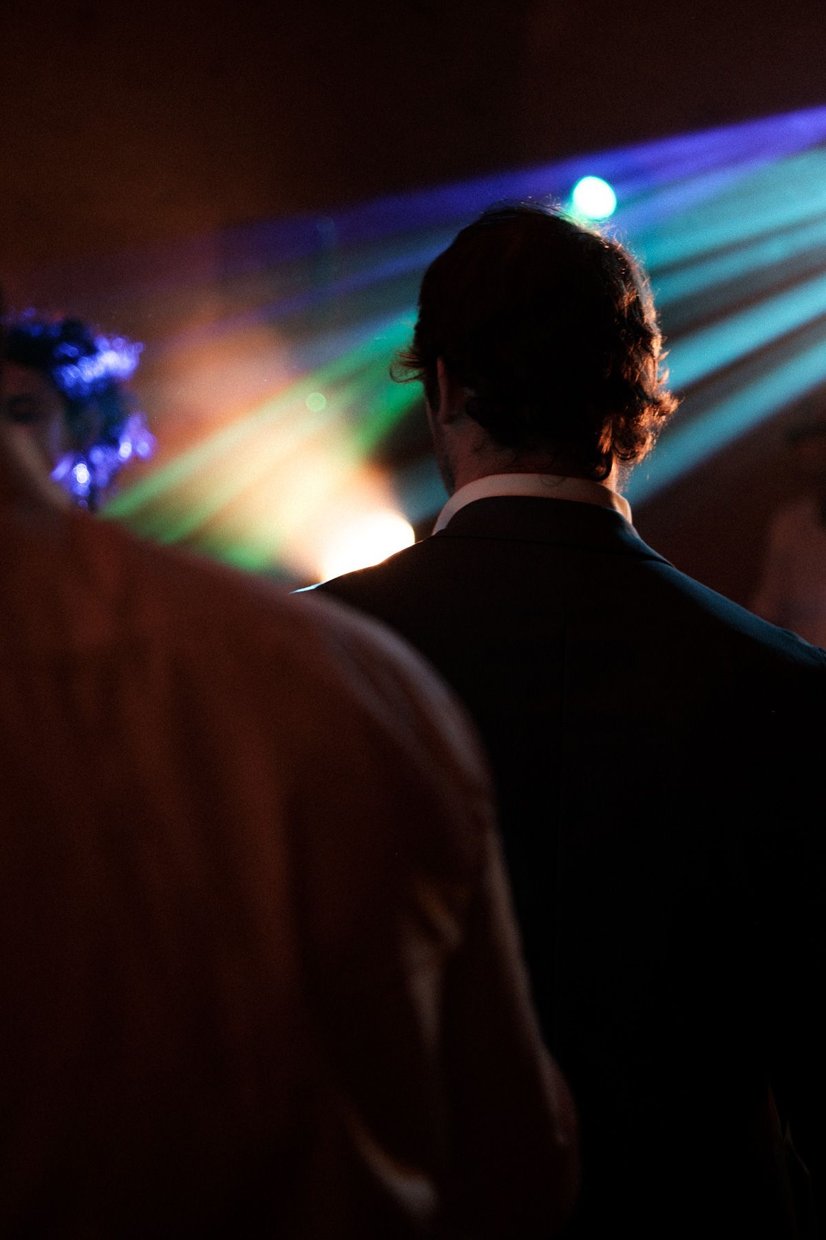 Silhouetted figures stand against a dark background with colorful blue and green stage lighting creating an atmospheric effect.