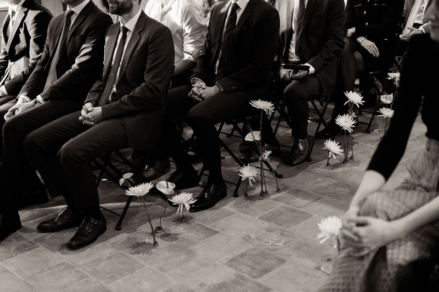 Black and white wedding photo showing guests' feet and legs seated in a row during a ceremony.