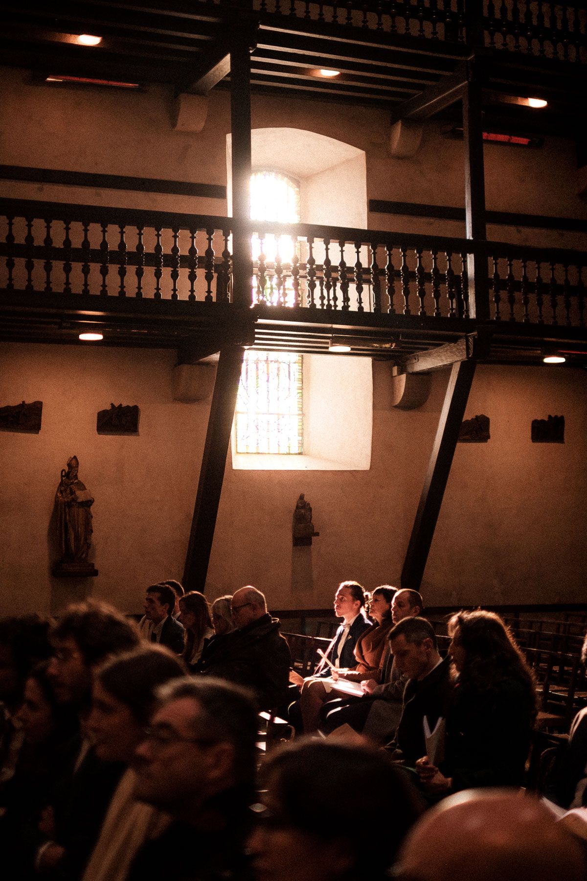 A dimly lit church interior with wooden balconies and people gathered in silhouette during a service.