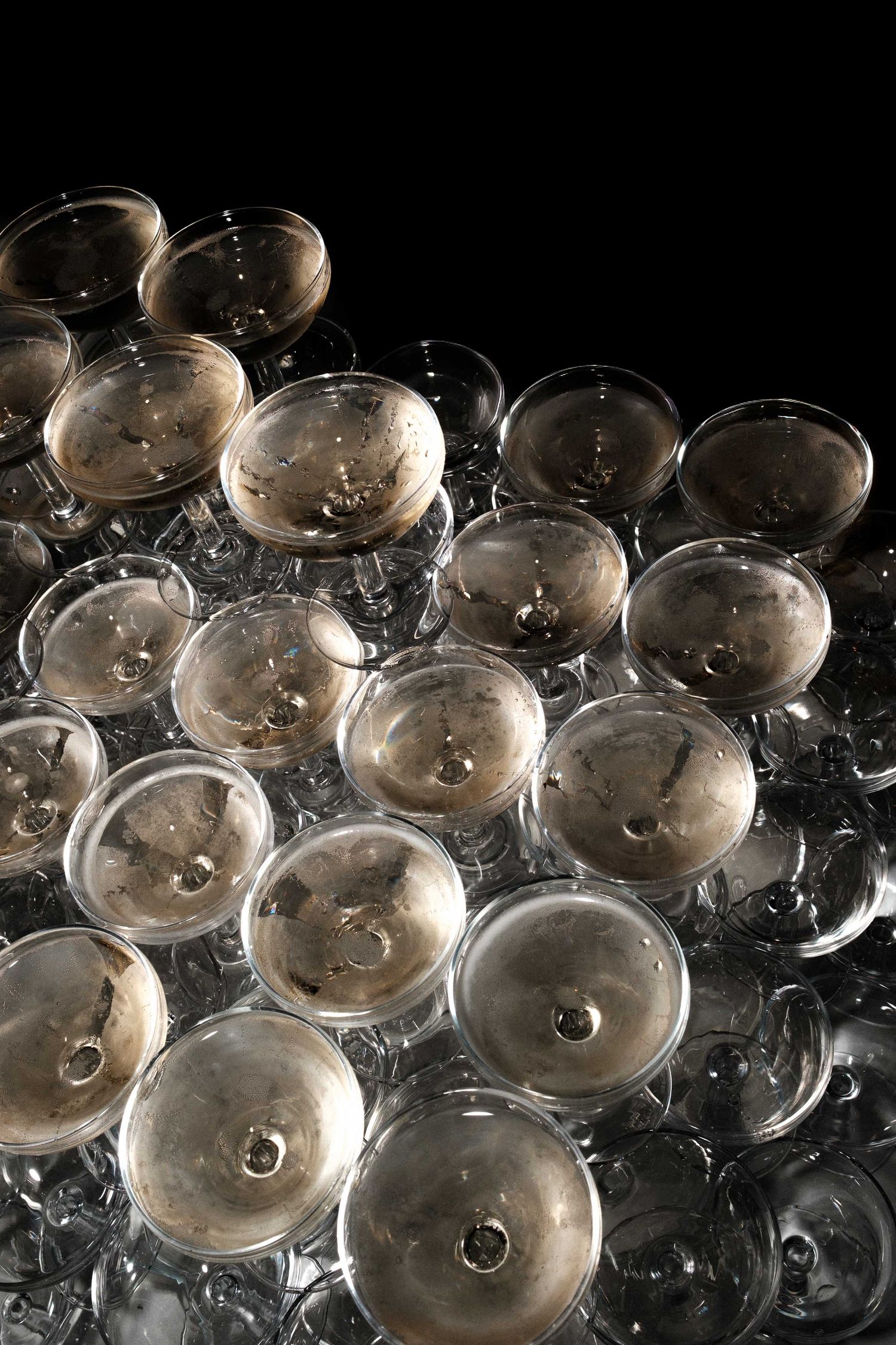Multiple empty champagne glasses arranged in rows on a dark background with dramatic lighting.