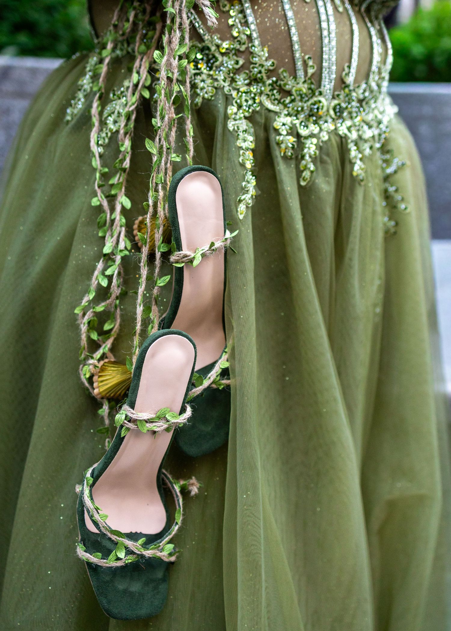 Green heeled sandals with floral vine details displayed against an olive green tulle gown with beaded embellishments.