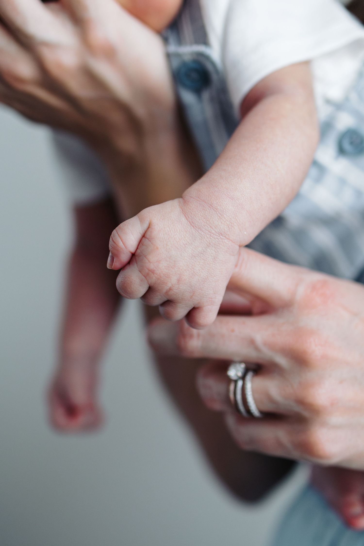 Close-up of a newborn baby's tiny hand grasping an adult's finger, with a diamond ring visible.