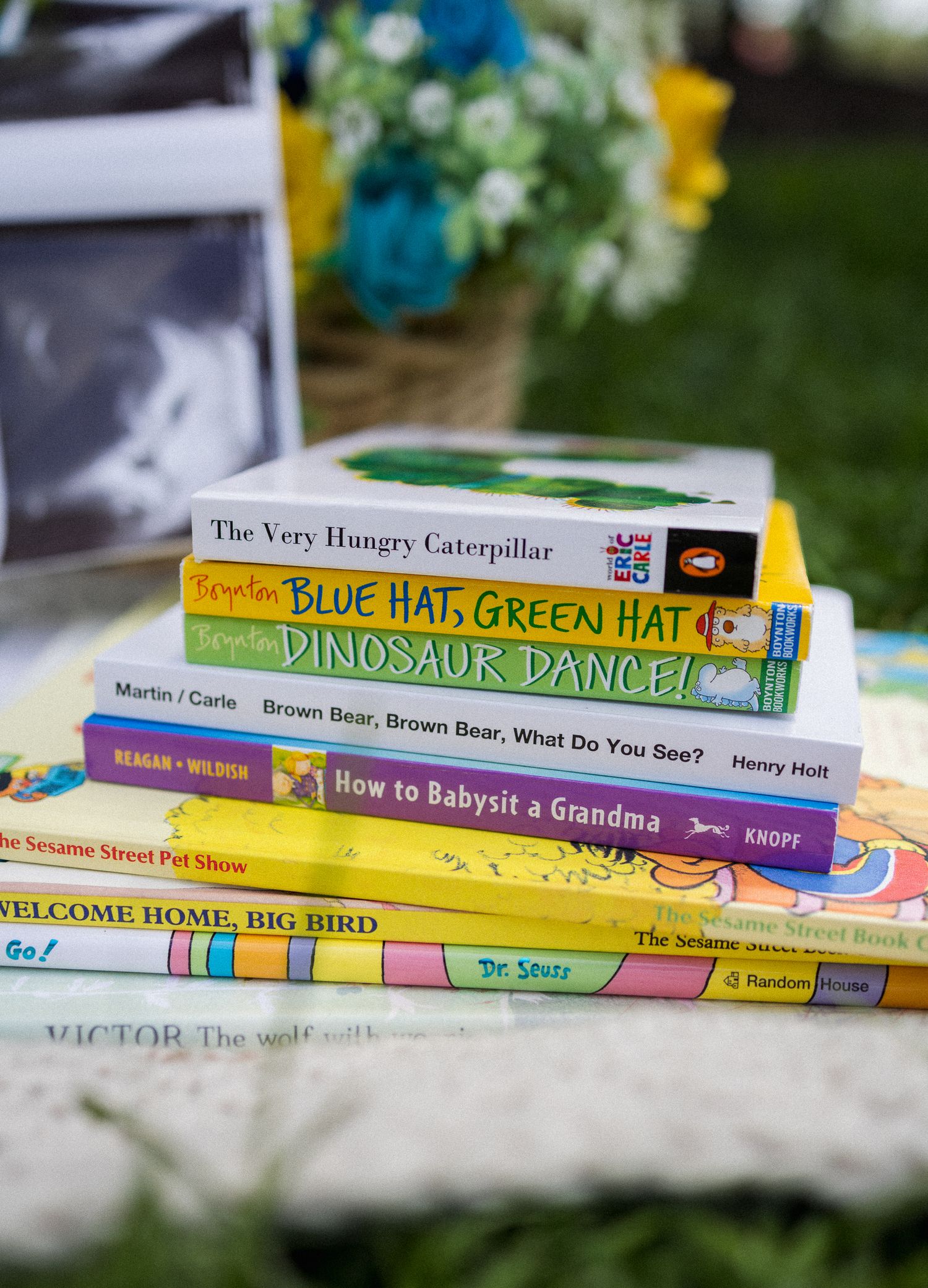 Stack of colorful children's books including The Very Hungry Caterpillar and Dinosaur Dance at an outdoor baby shower.