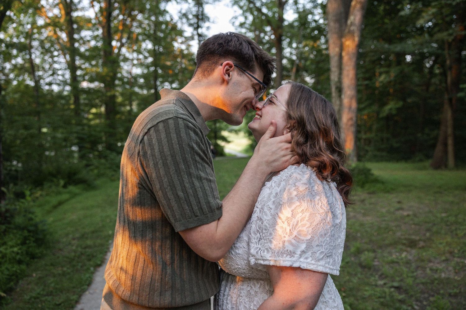 Couple sharing a romantic moment outdoors in golden hour light, surrounded by lush green trees.