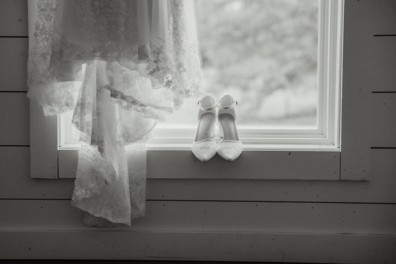 White bridal heels and lace wedding gown displayed on window sill in black and white.