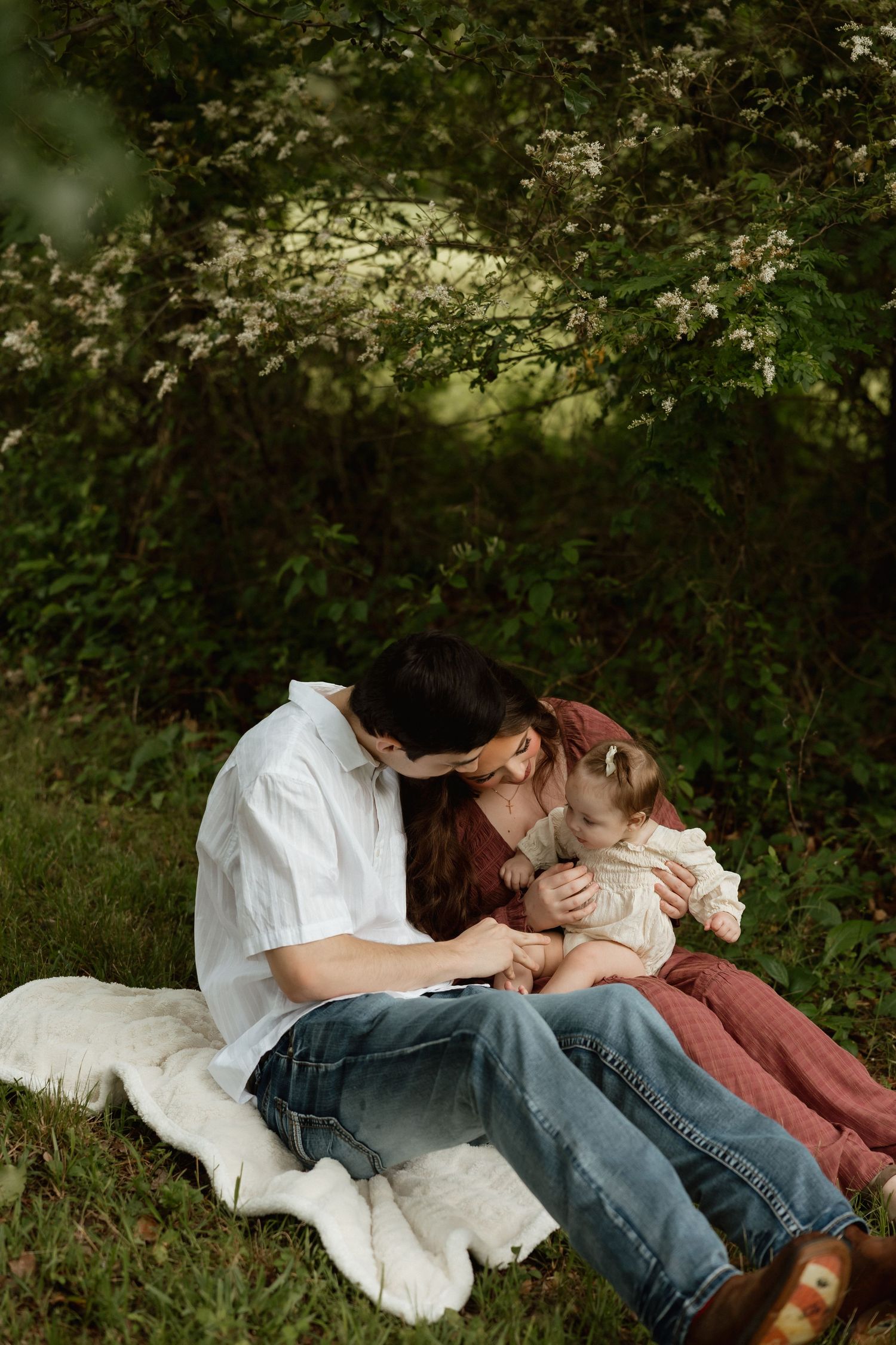 Couple sitting on blanket outdoors lovingly attending to toddler.