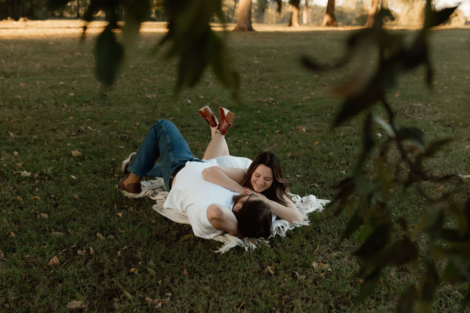 Romantic couple lying together on a blanket in a grassy park, relaxing in the warm golden hour light.