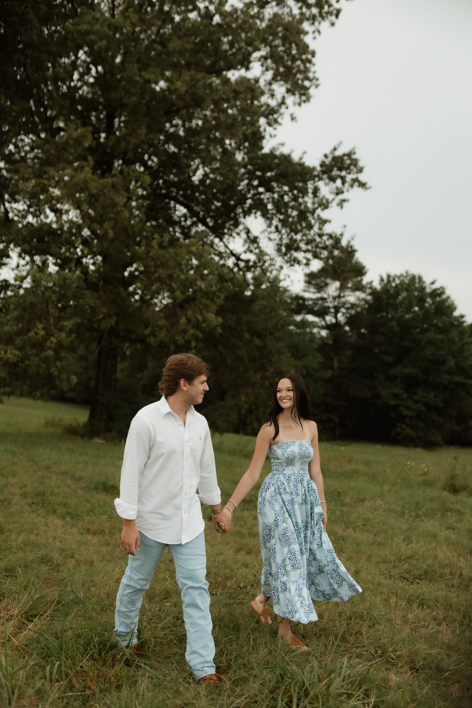 A happy couple holds hands and walks through a lush green field, smiling at each other.