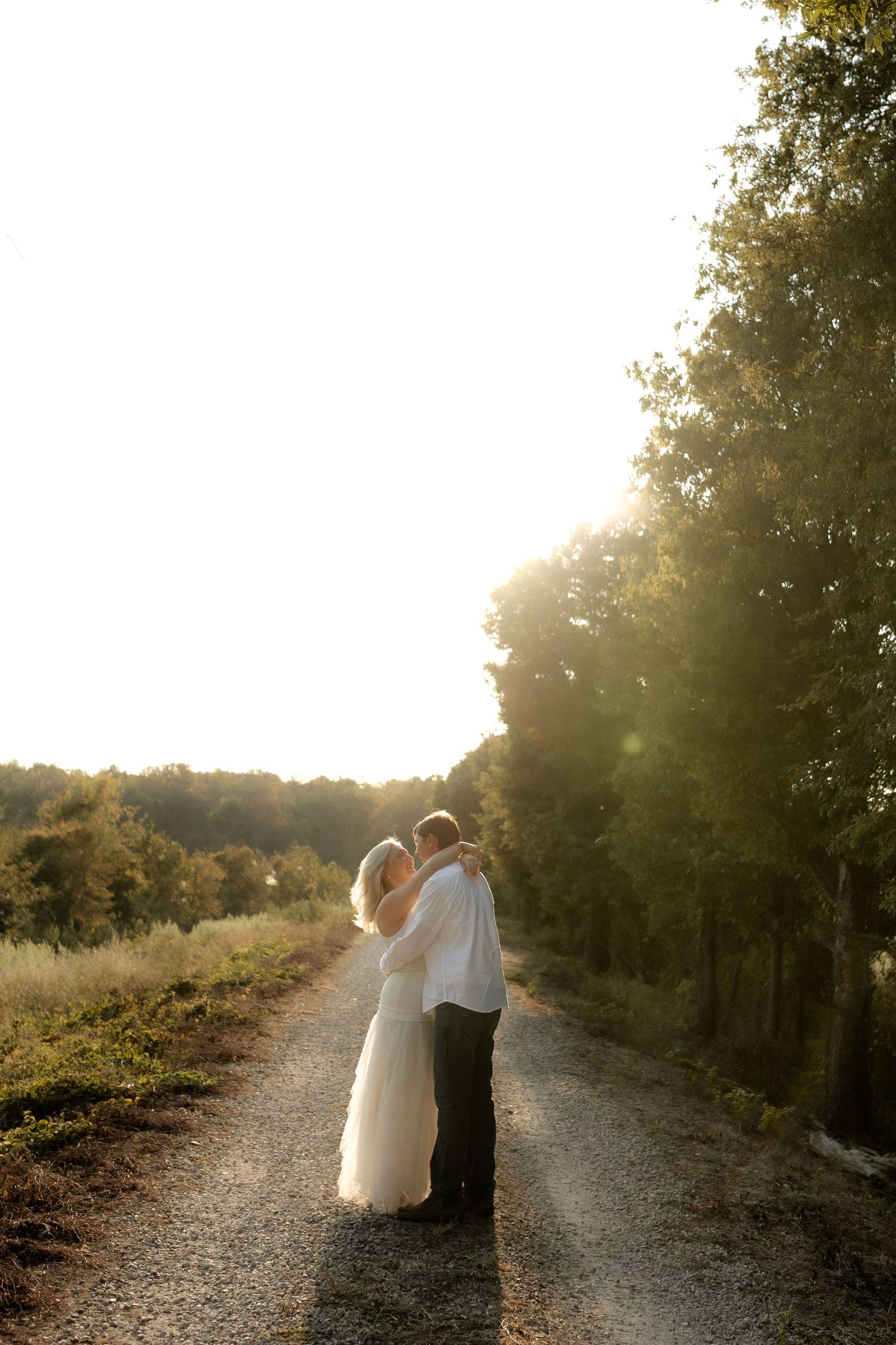 Couple embracing on a gravel path surrounded by trees in beautiful golden sunset backlight.