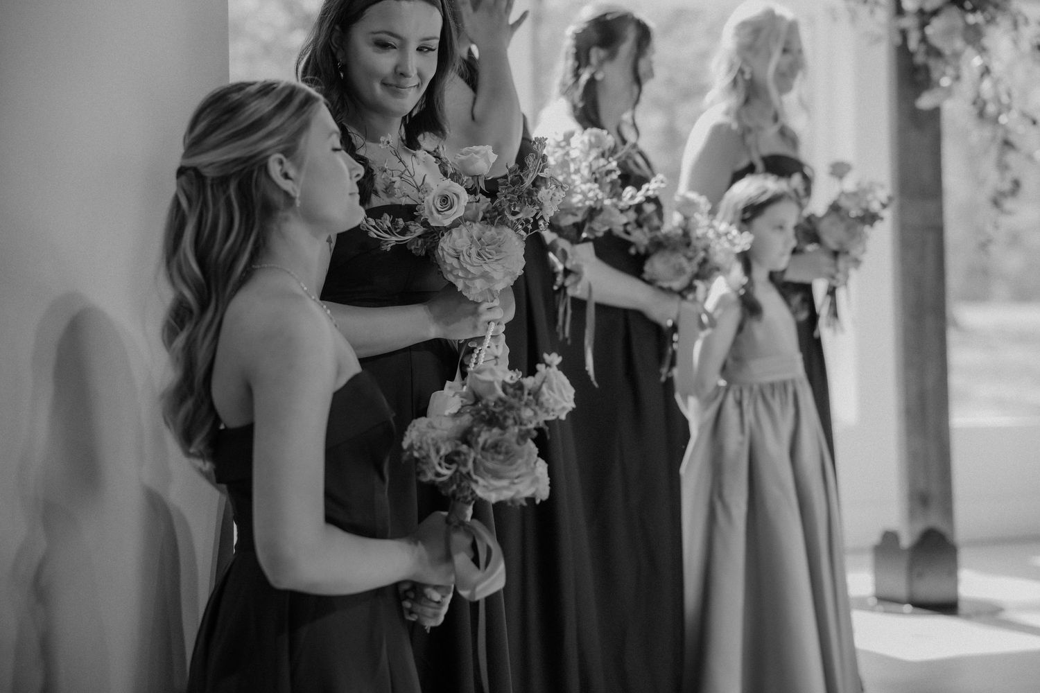 Bridesmaids in dark dresses holding beautiful floral bouquets before wedding ceremony.