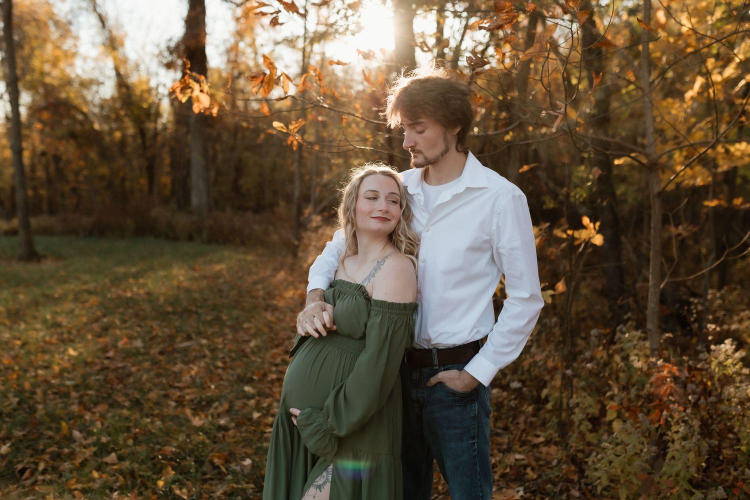 Couple sharing a tender moment outdoors, pregnant woman in green gown with partner in autumn sunlight.