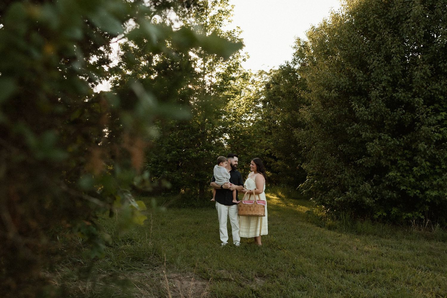 Couple standing together in a lush green forest clearing during golden hour sunset light.