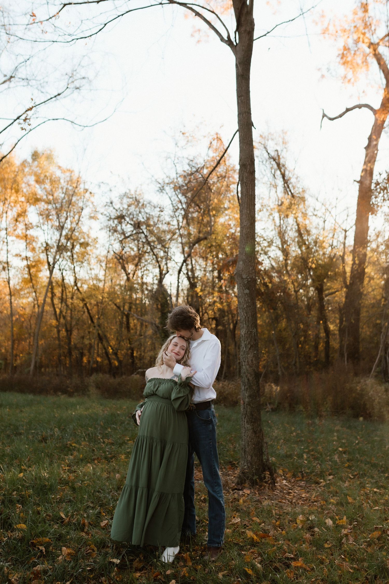 Couple embracing near a tree in an autumn park, pregnant woman in elegant green maternity dress.