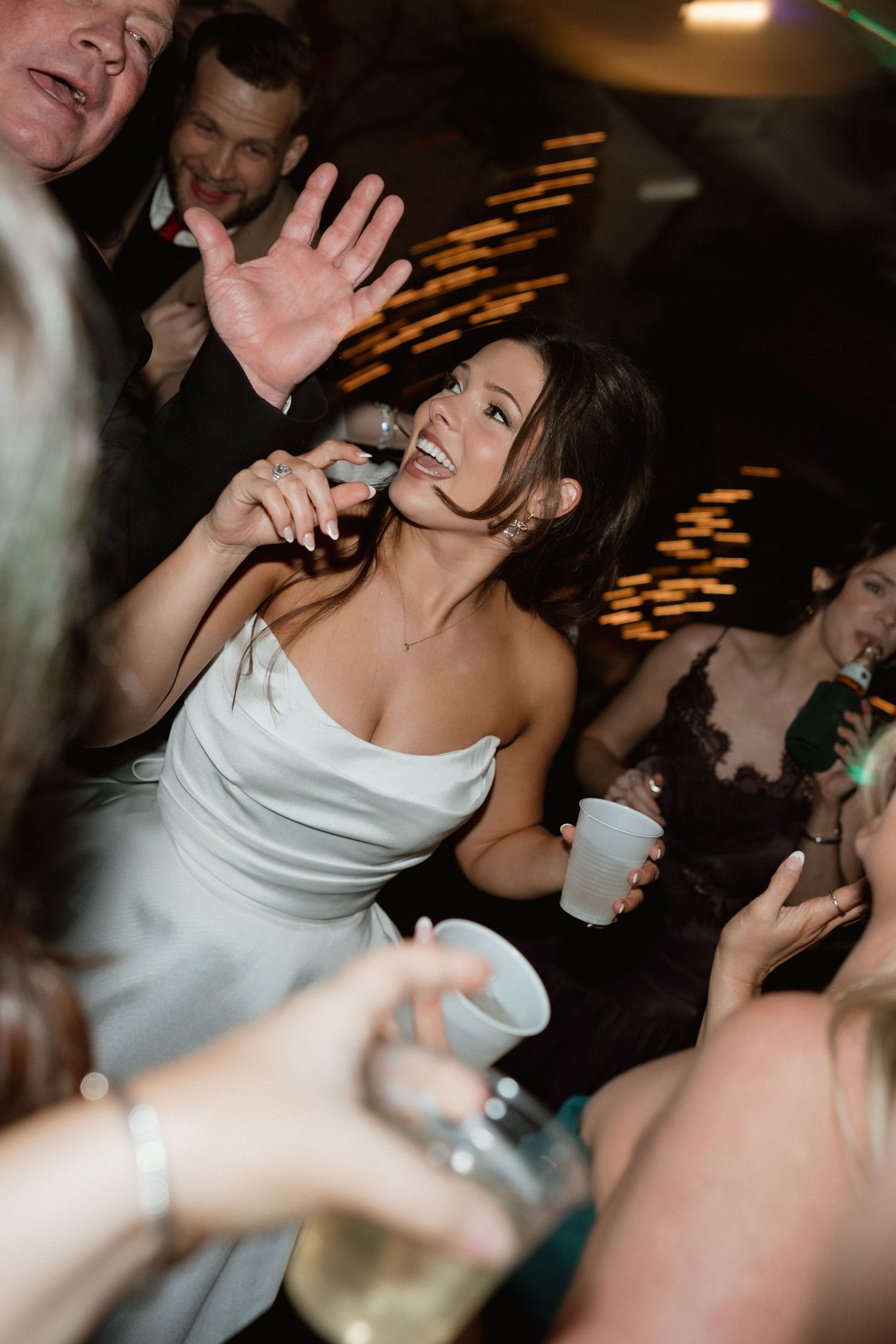Bride in white strapless gown laughing and dancing at wedding reception.