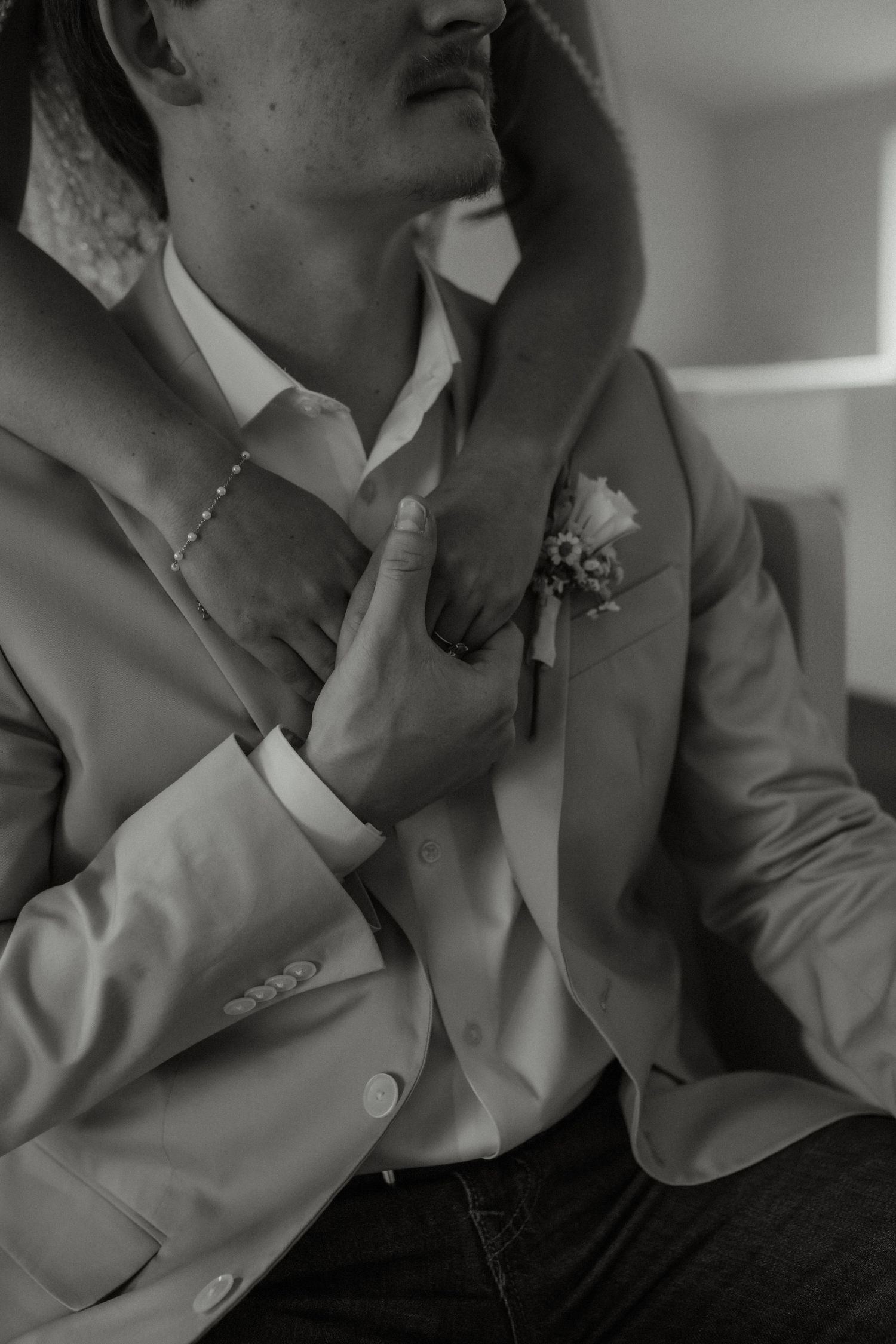 Black and white close-up of groom in suit with boutonniere as bride tenderly touches his face and chest.