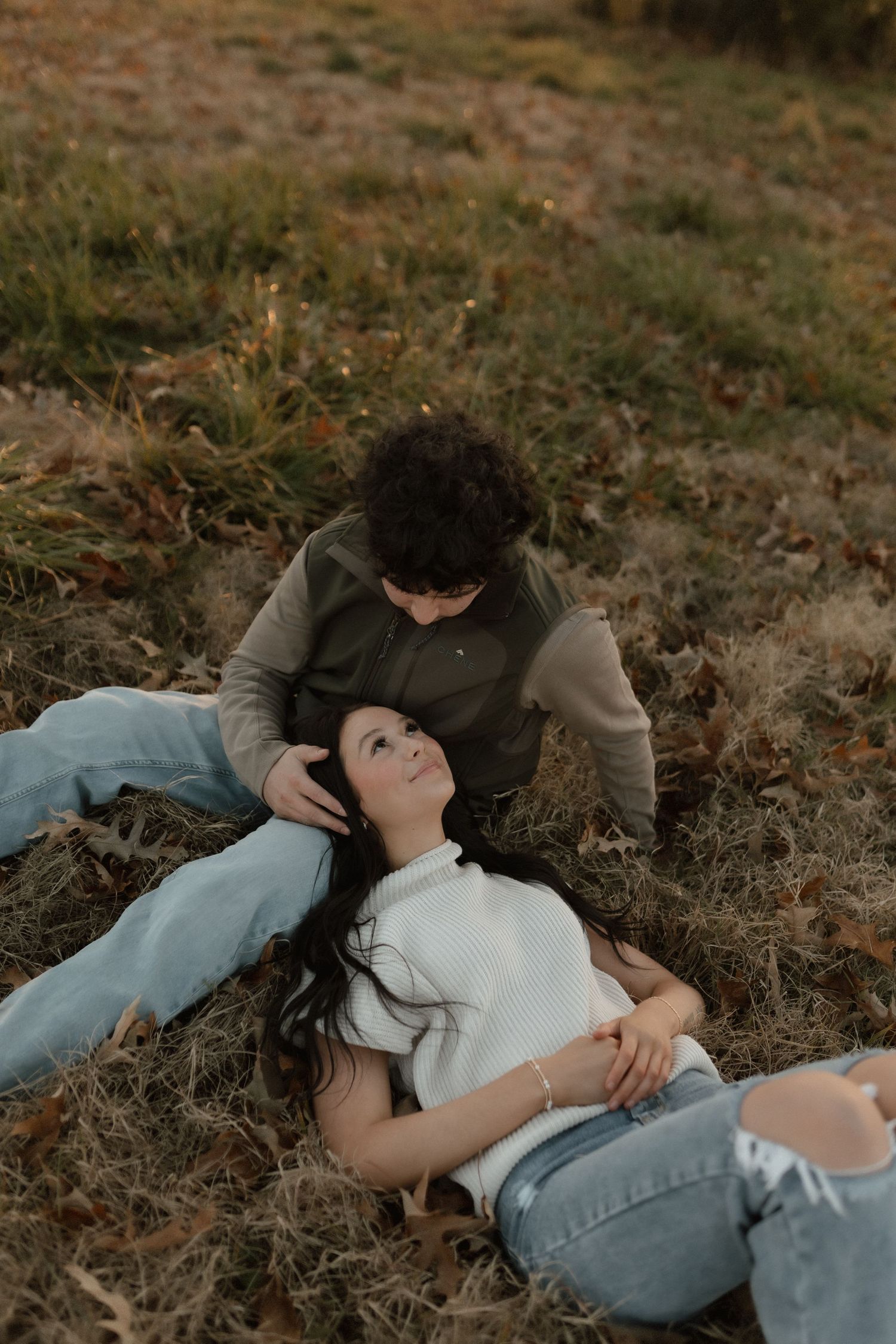 A couple relaxes on autumn grass, woman lying with head near mans lap at sunset.