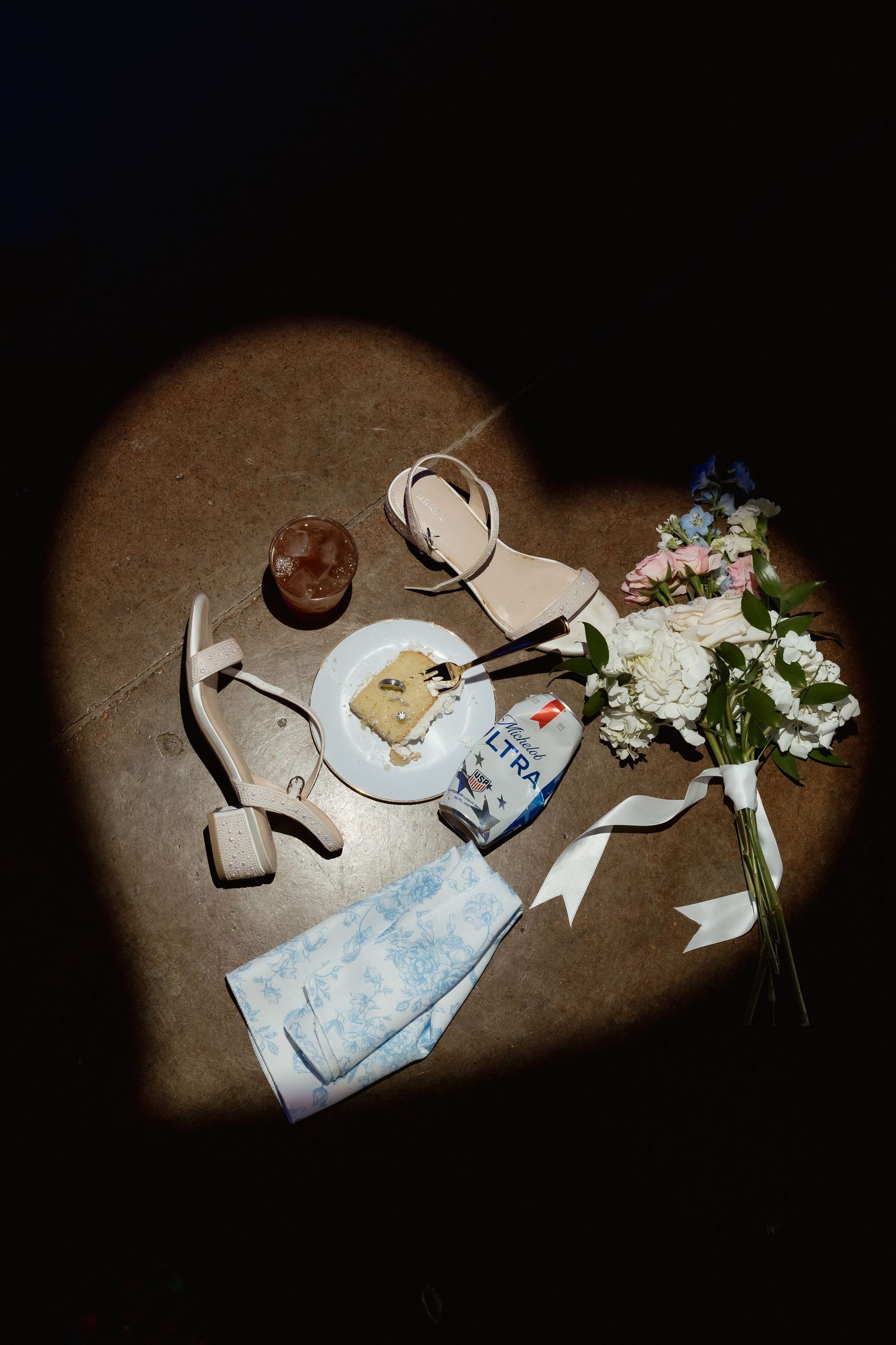 Heart-shaped spotlight on wedding shoes, bouquet, cake, and accessories on dance floor.