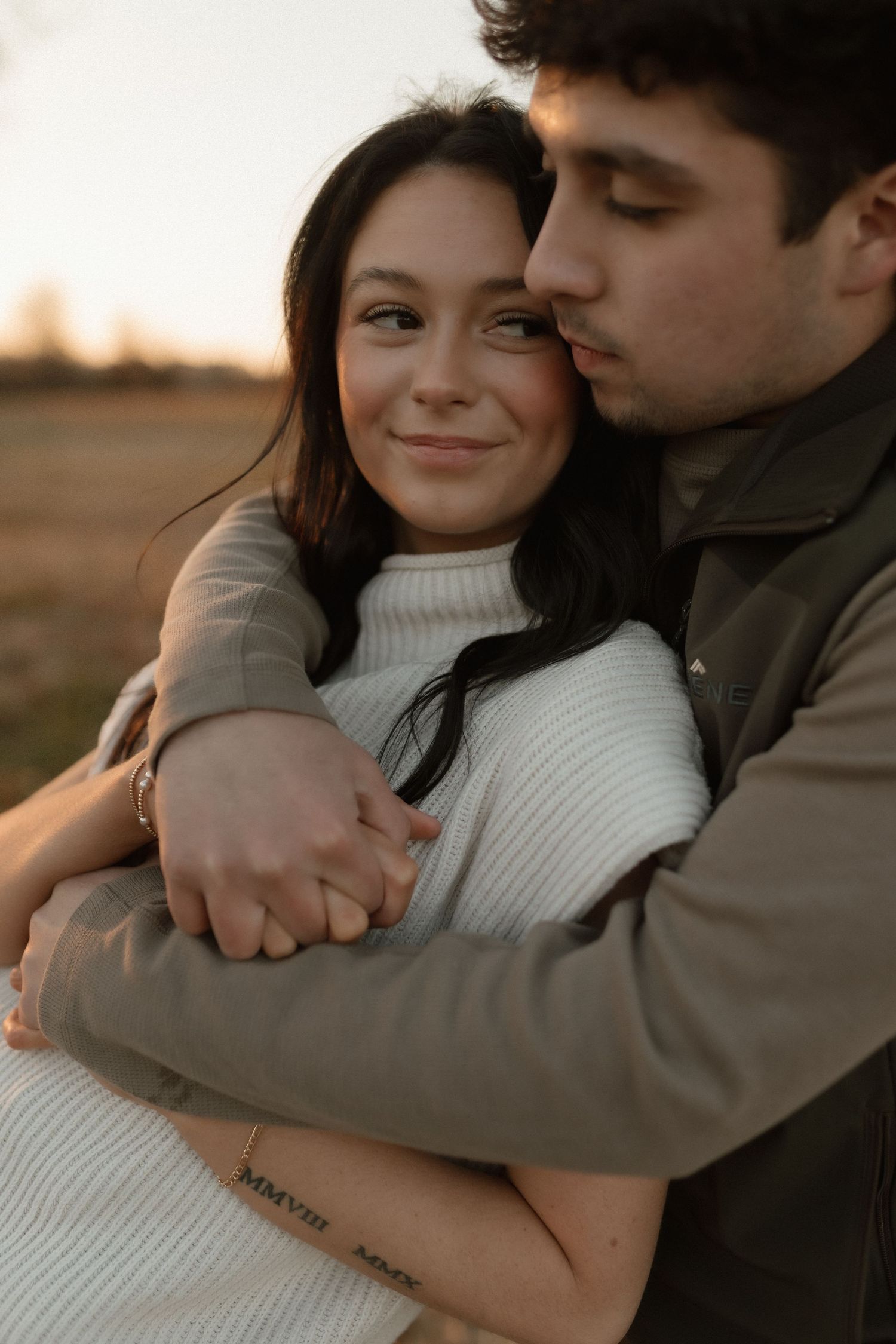 A man kisses a smiling womans cheek while embracing her warmly at golden hour sunset.