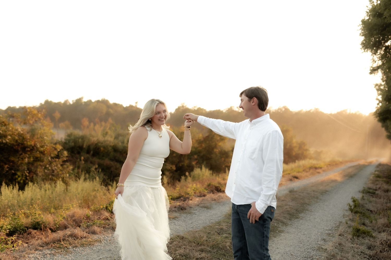 Couple dancing joyfully on a dusty gravel road during a golden sunset.