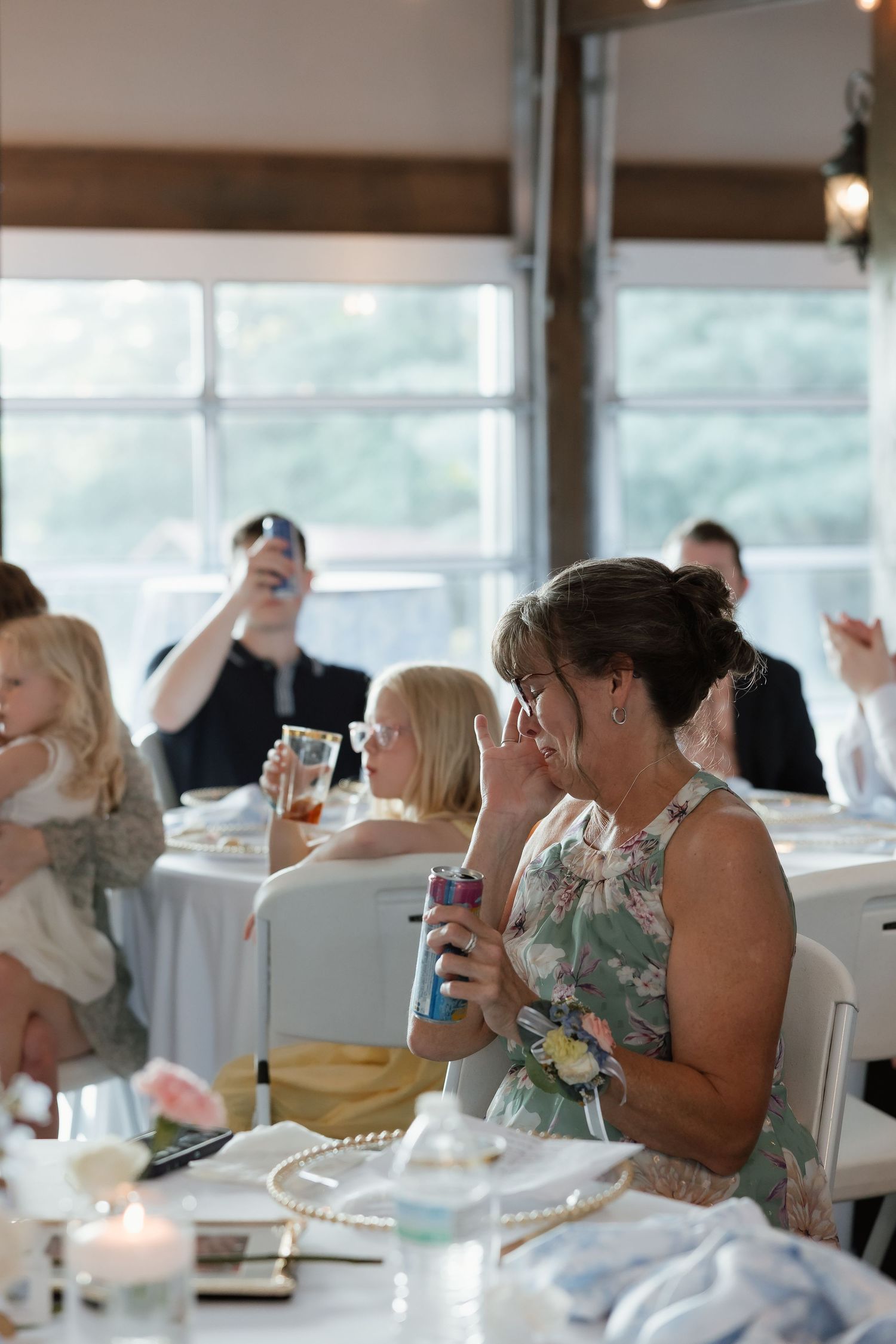 Wedding guest in floral dress wiping tears during emotional wedding reception speech.