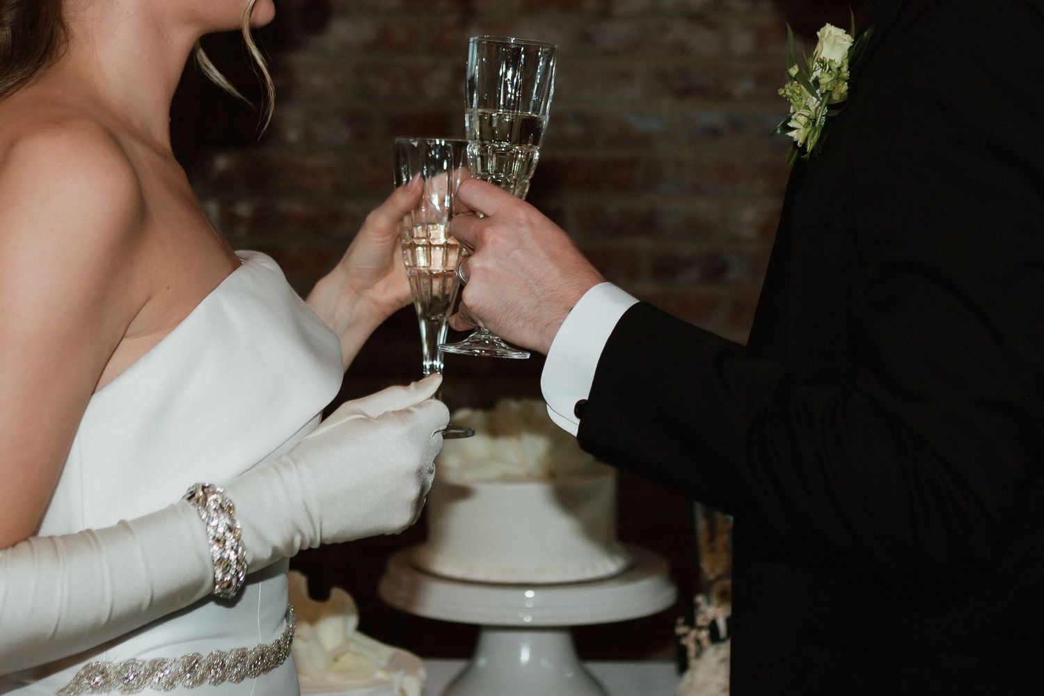 Bride and groom toasting with champagne flutes in front of a white wedding cake.