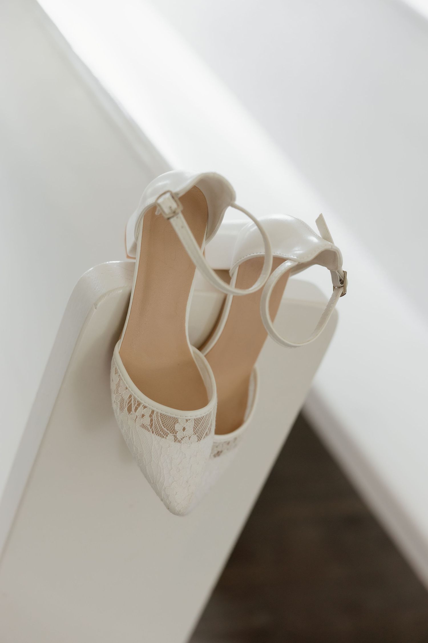 Elegant white lace bridal heels with ankle strap displayed on white surface.