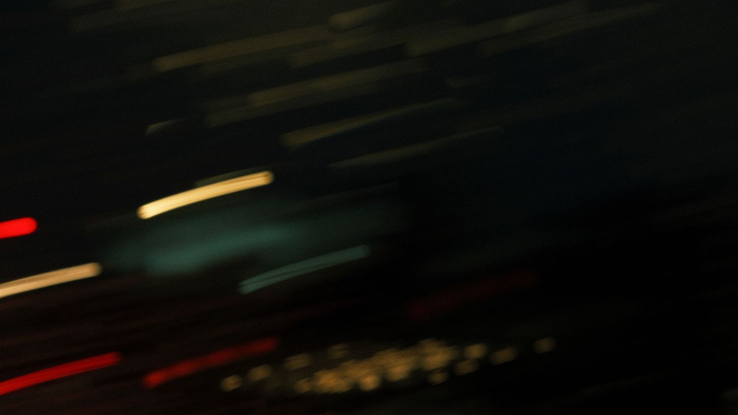 Dark abstract night photography with blurred streaks of colorful city lights in motion.