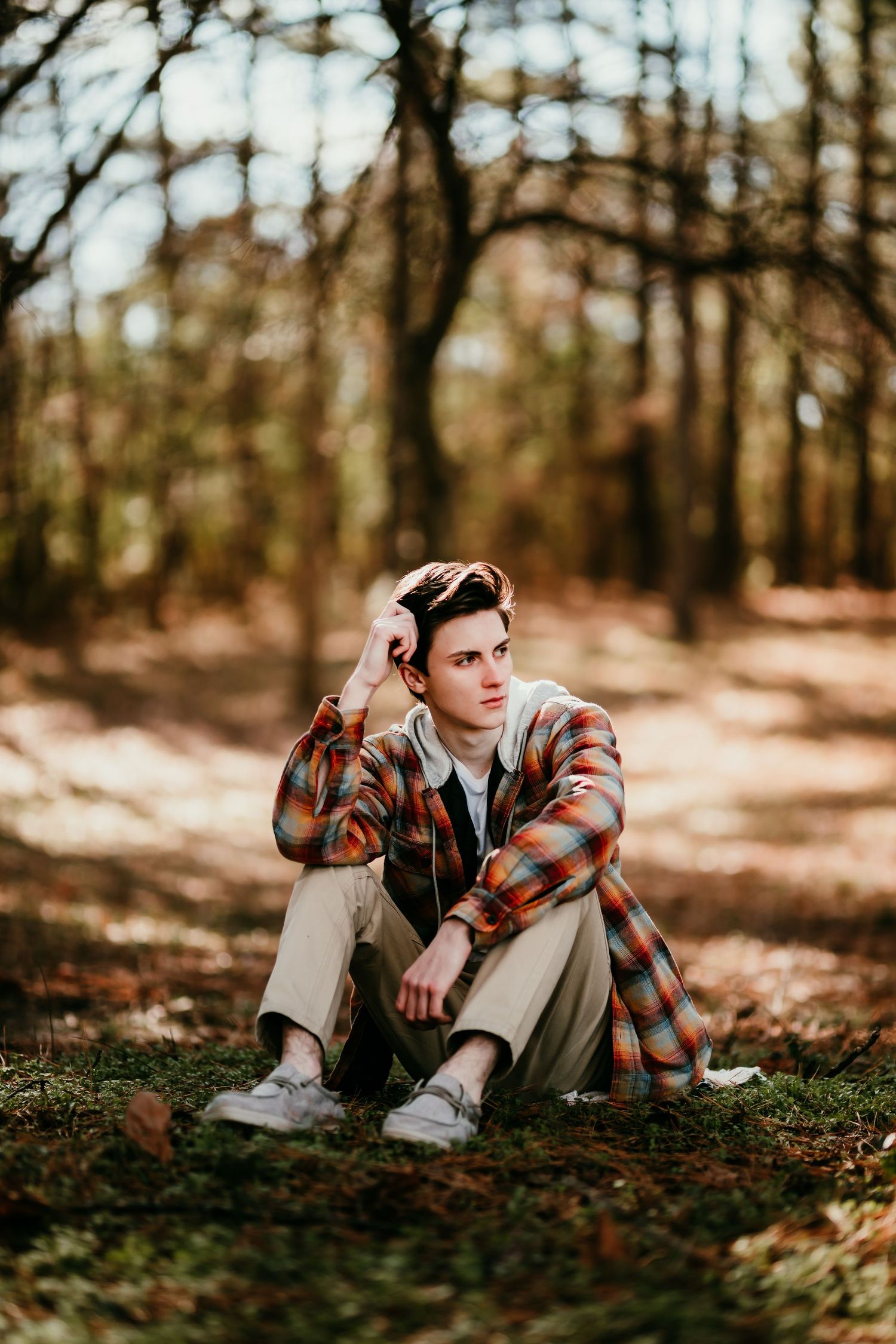 Young man in plaid shirt sitting on grass in wooded forest path during fall.