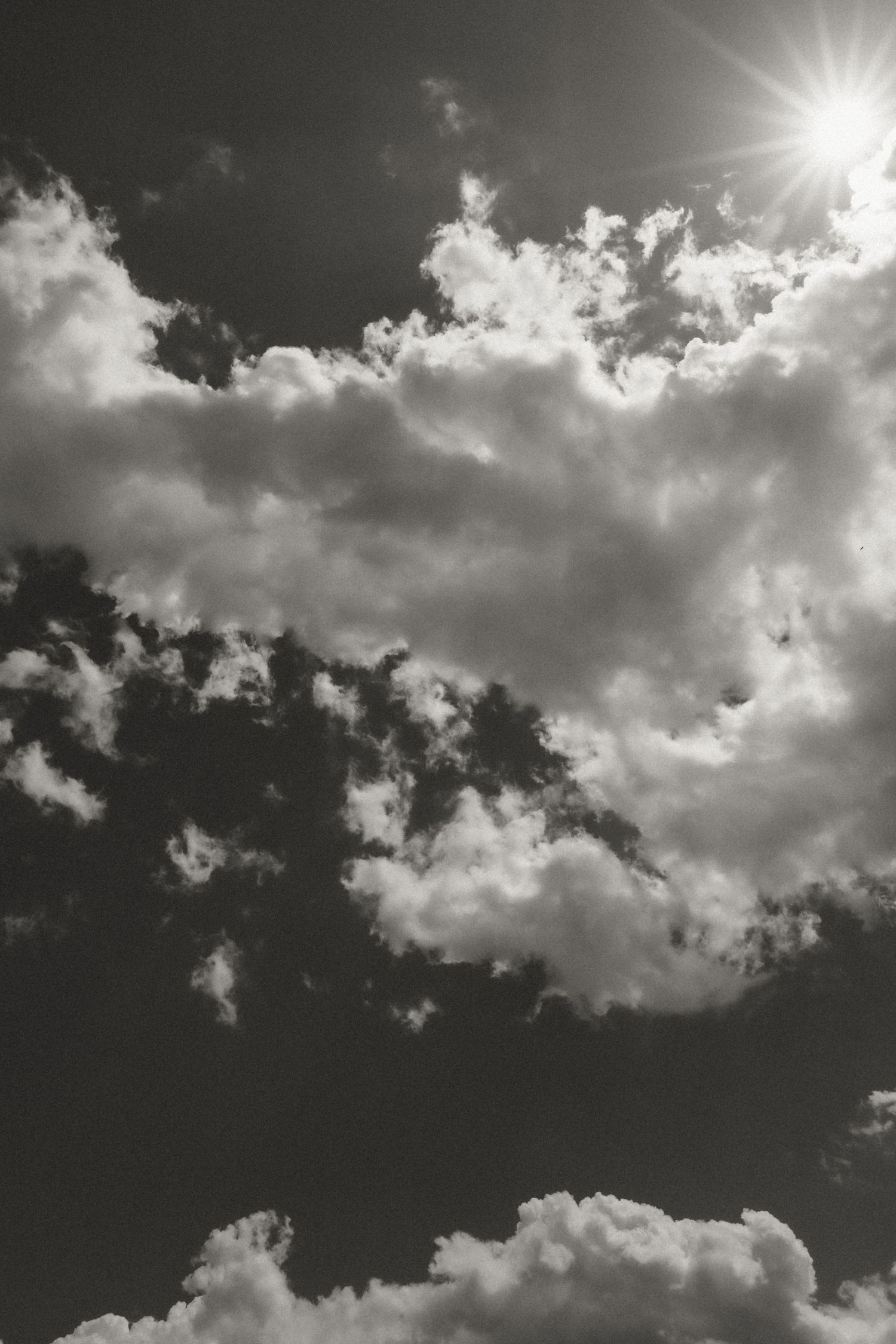 Dramatic black and white sky with sunburst breaking through fluffy clouds, moody nature photography.