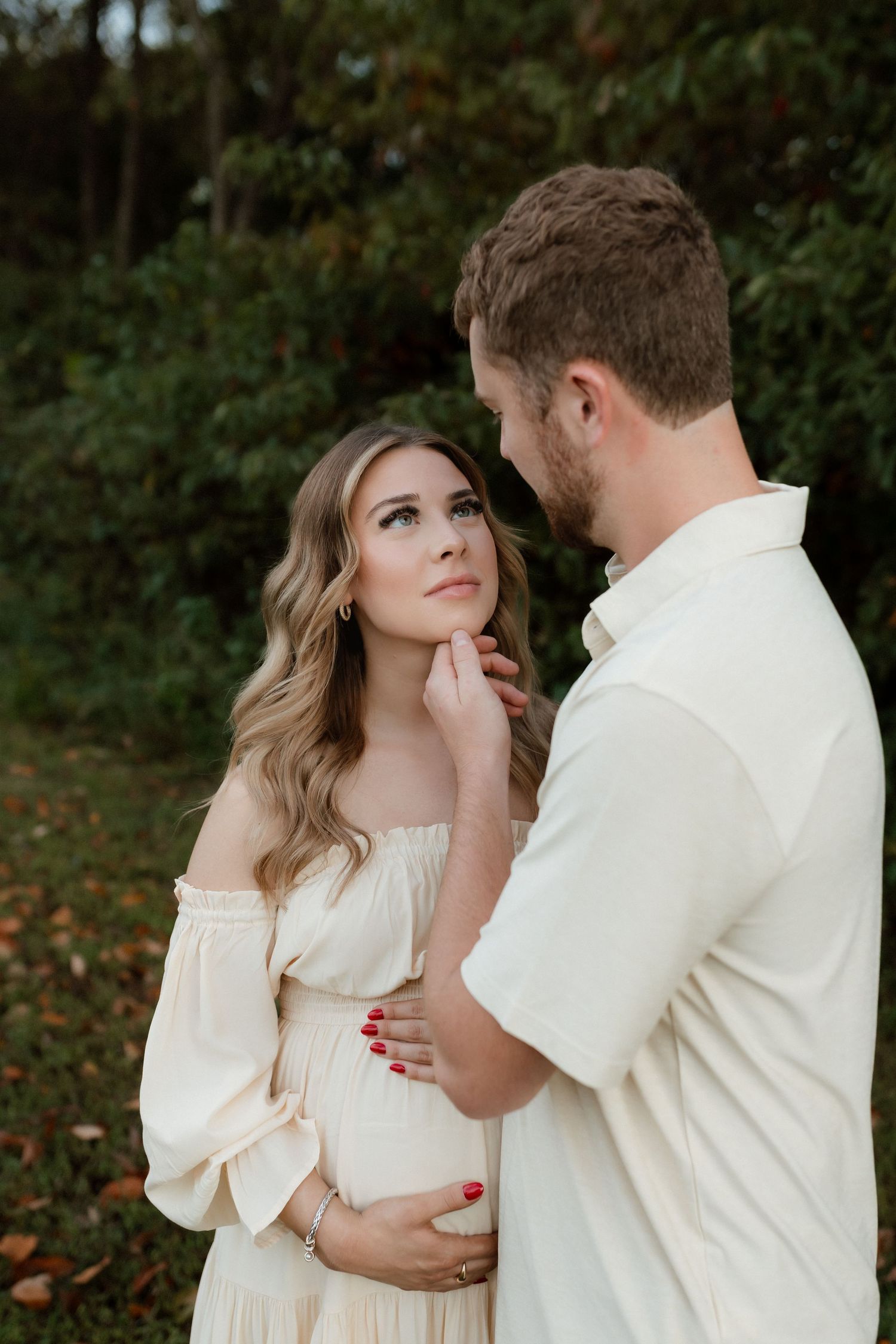 Couple shares tender moment outdoors, man gently touching pregnant womans chin in nature.