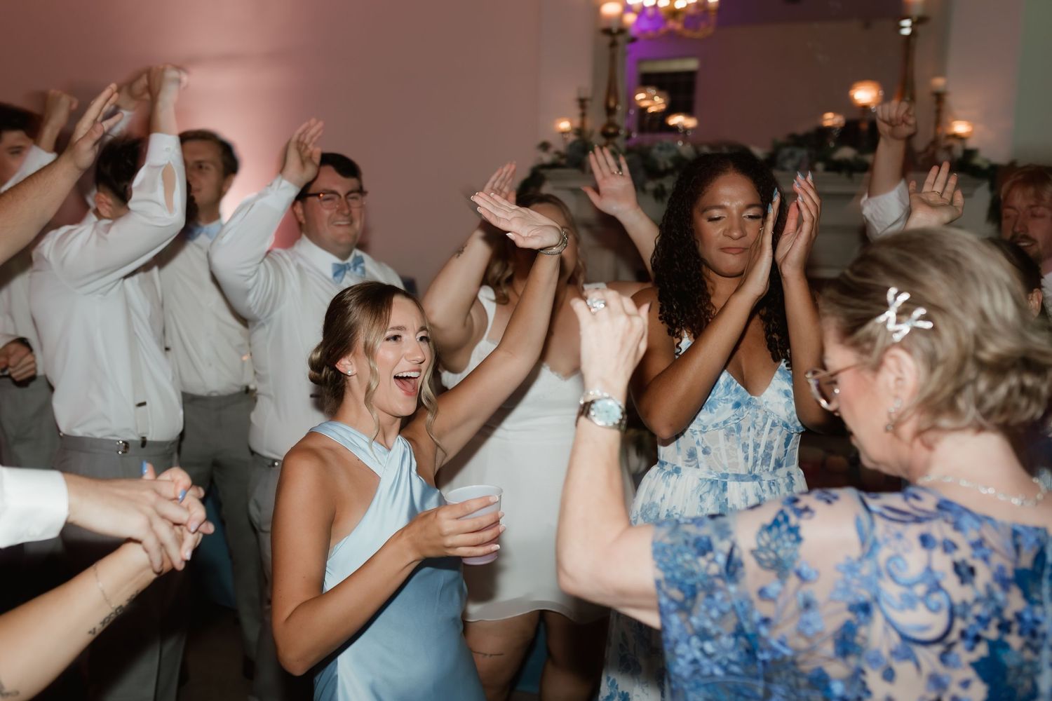 Energetic wedding reception dance floor with guests celebrating and raising their hands joyfully.