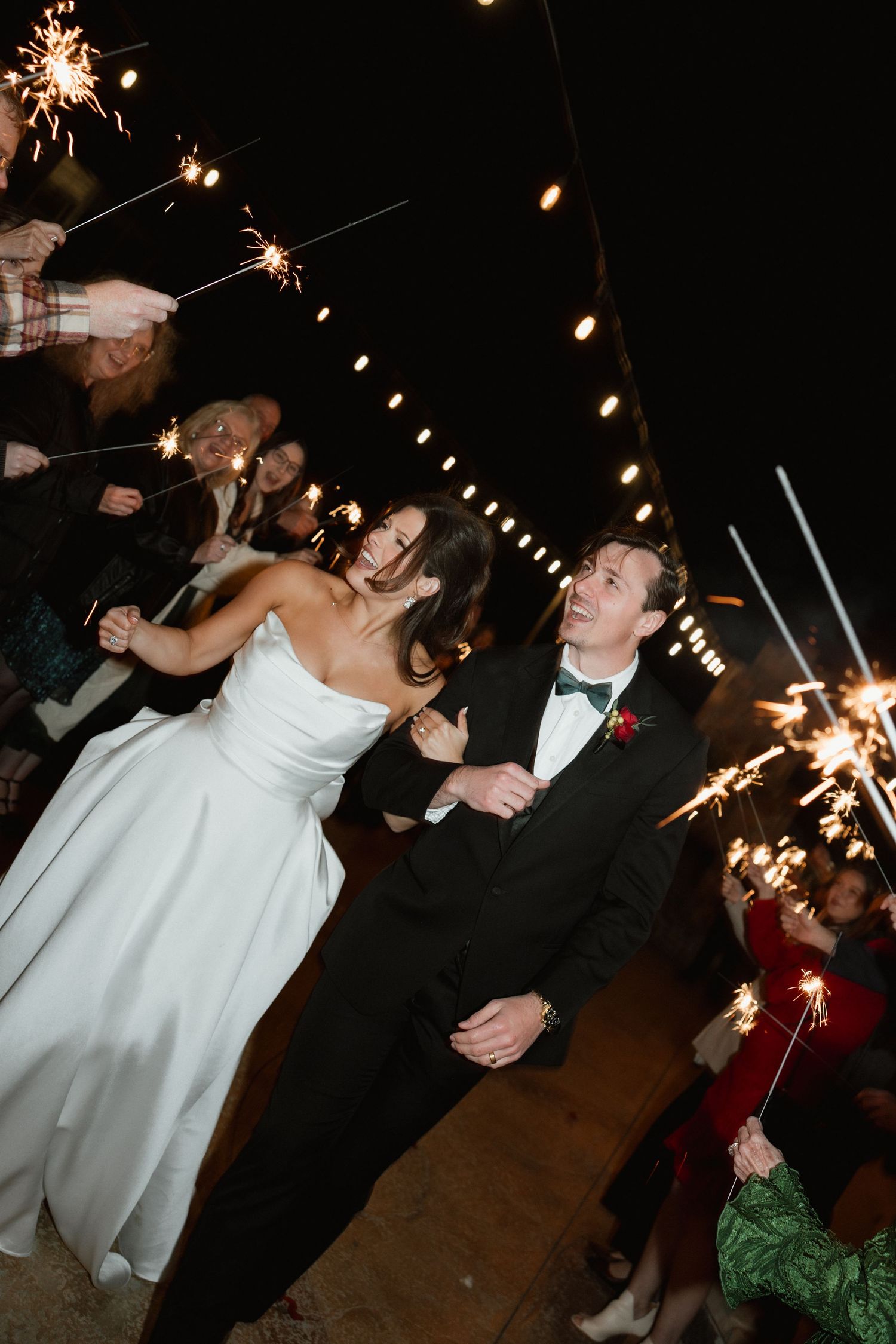 Bride and groom walking through sparkler send-off tunnel at night wedding reception.