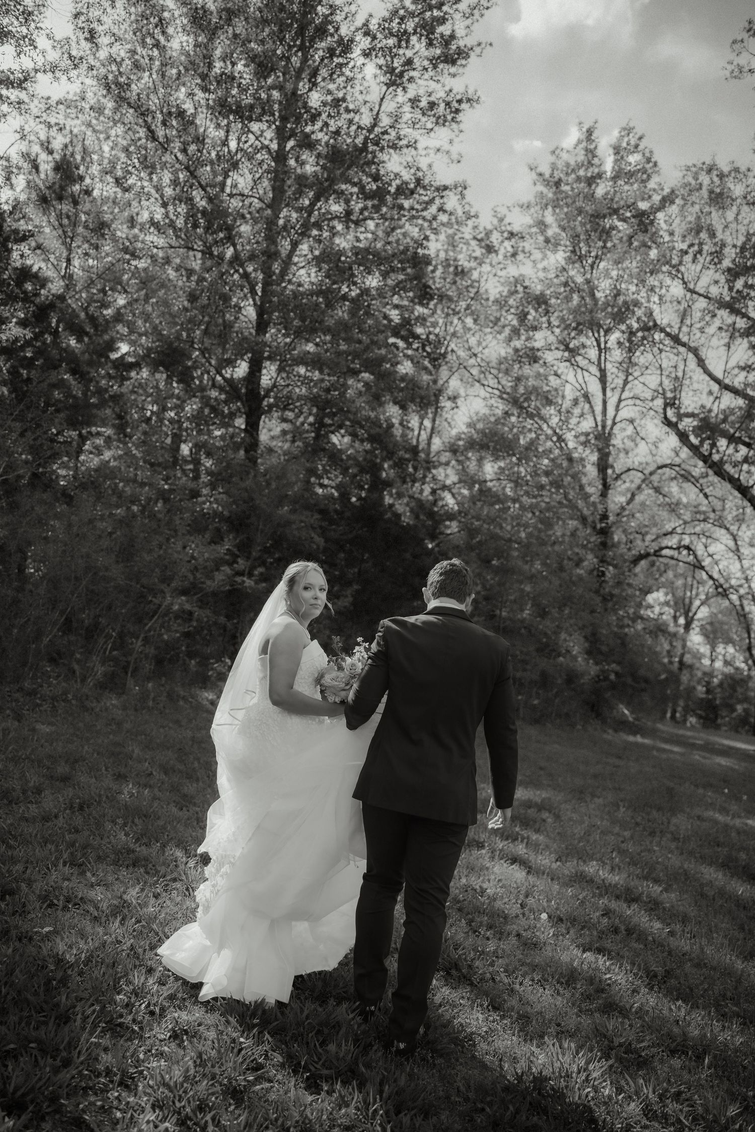 Bride and groom walking hand in hand through lush green field after wedding.