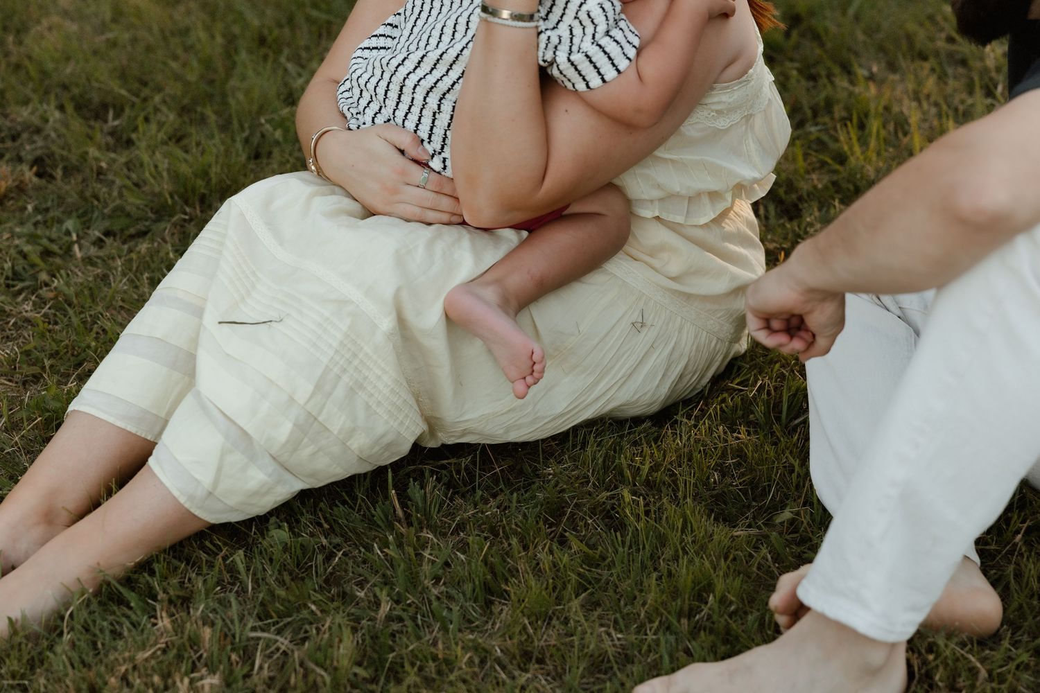 Close-up of mother holding baby on grass while father reaches out to touch baby's hand.