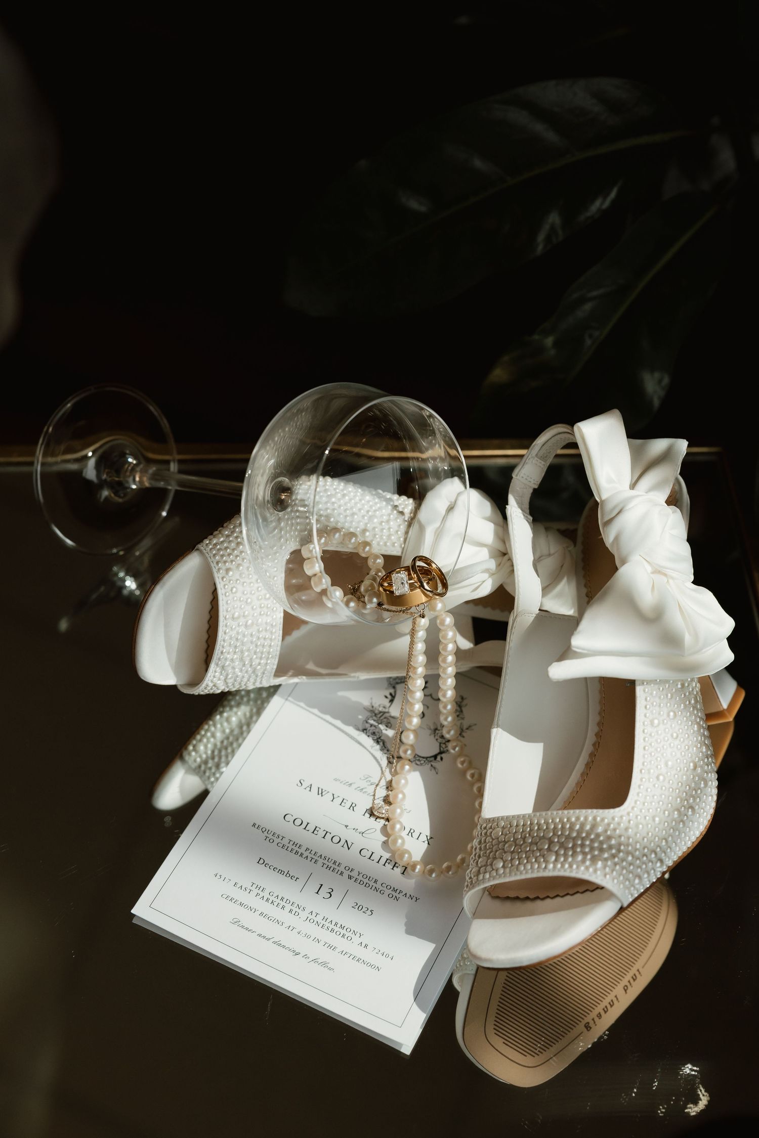 Elegant flat lay of pearl bridal heels, wedding invitation, rings, and pearl drop earrings.
