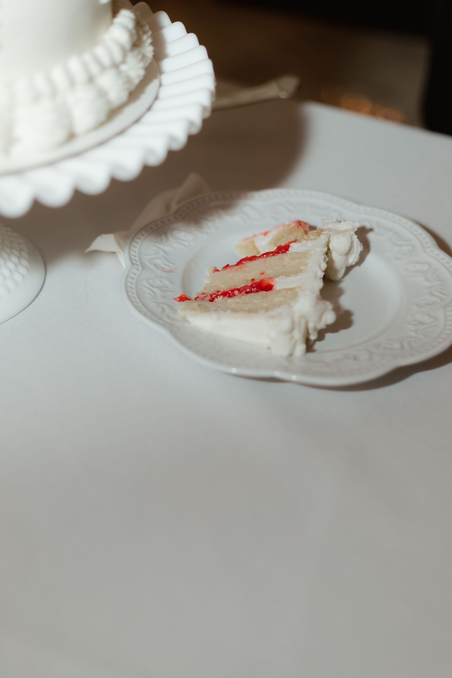 Slice of white wedding cake with red berry filling served on a decorative white plate.