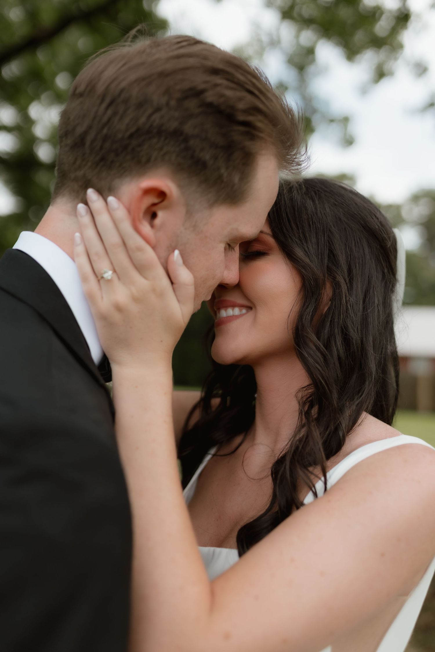 Bride smiles as she gently holds grooms face while sharing an intimate moment during their wedding.