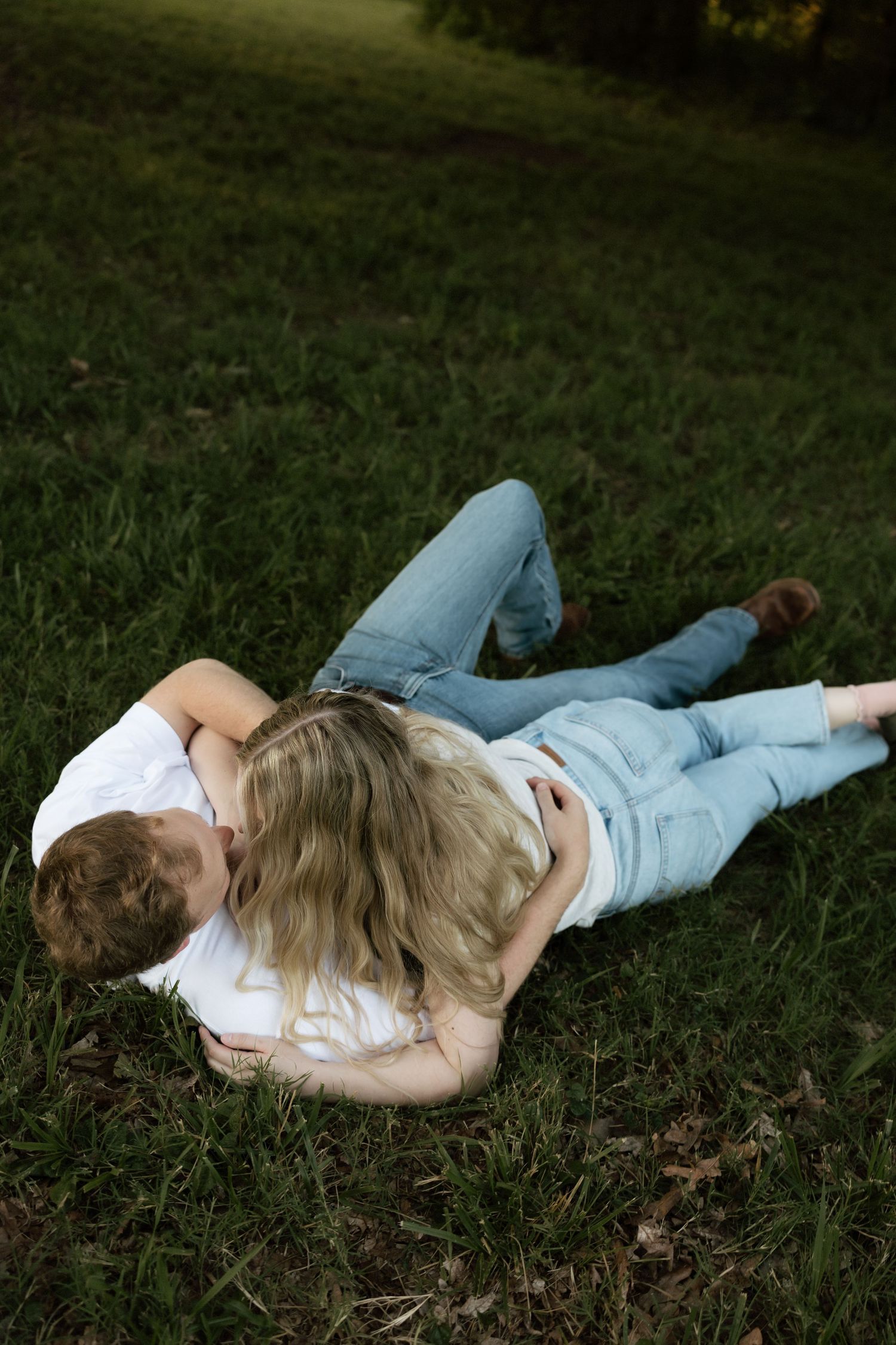 A couple embracing and cuddling together on a lush green grass lawn in a park setting.