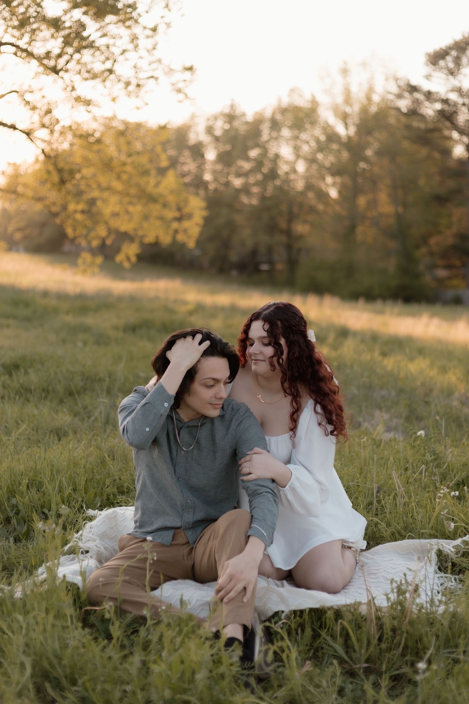 A couple sits together on a blanket in a sunlit meadow during golden hour sunset.