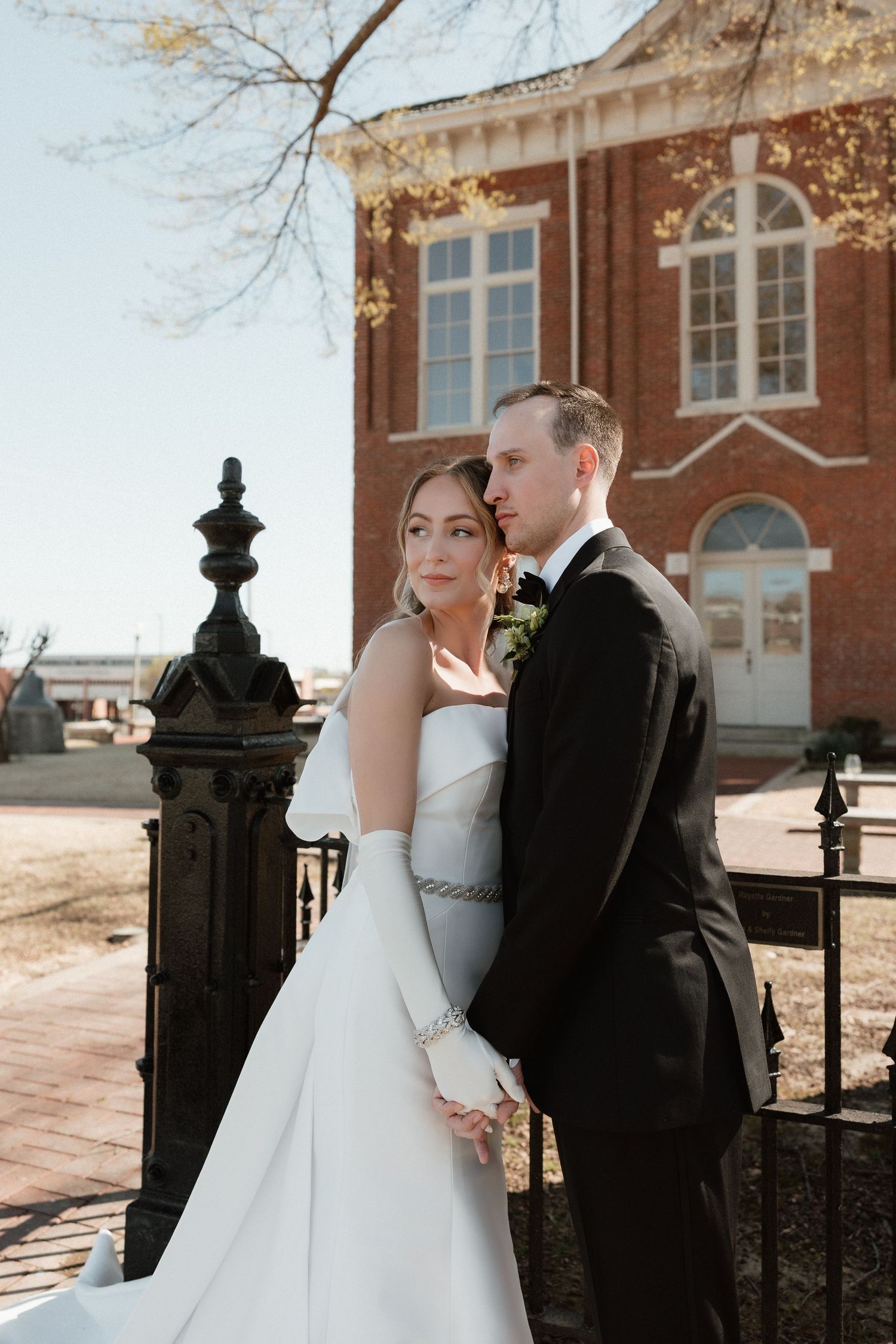 Bride and groom pose together outside a historic brick building on their wedding day.