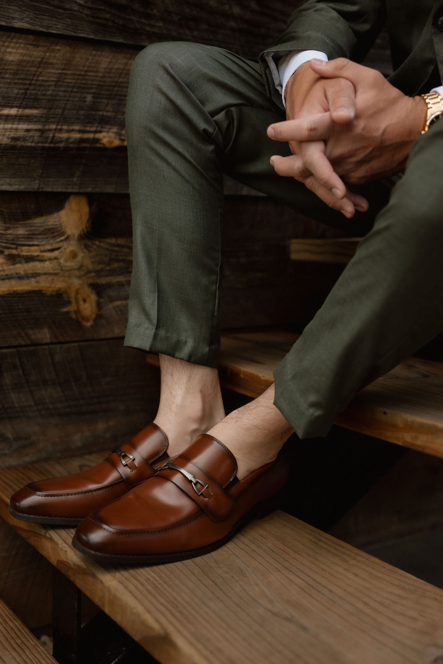 Groom in olive green suit sitting on wooden steps wearing brown leather monk strap loafers.