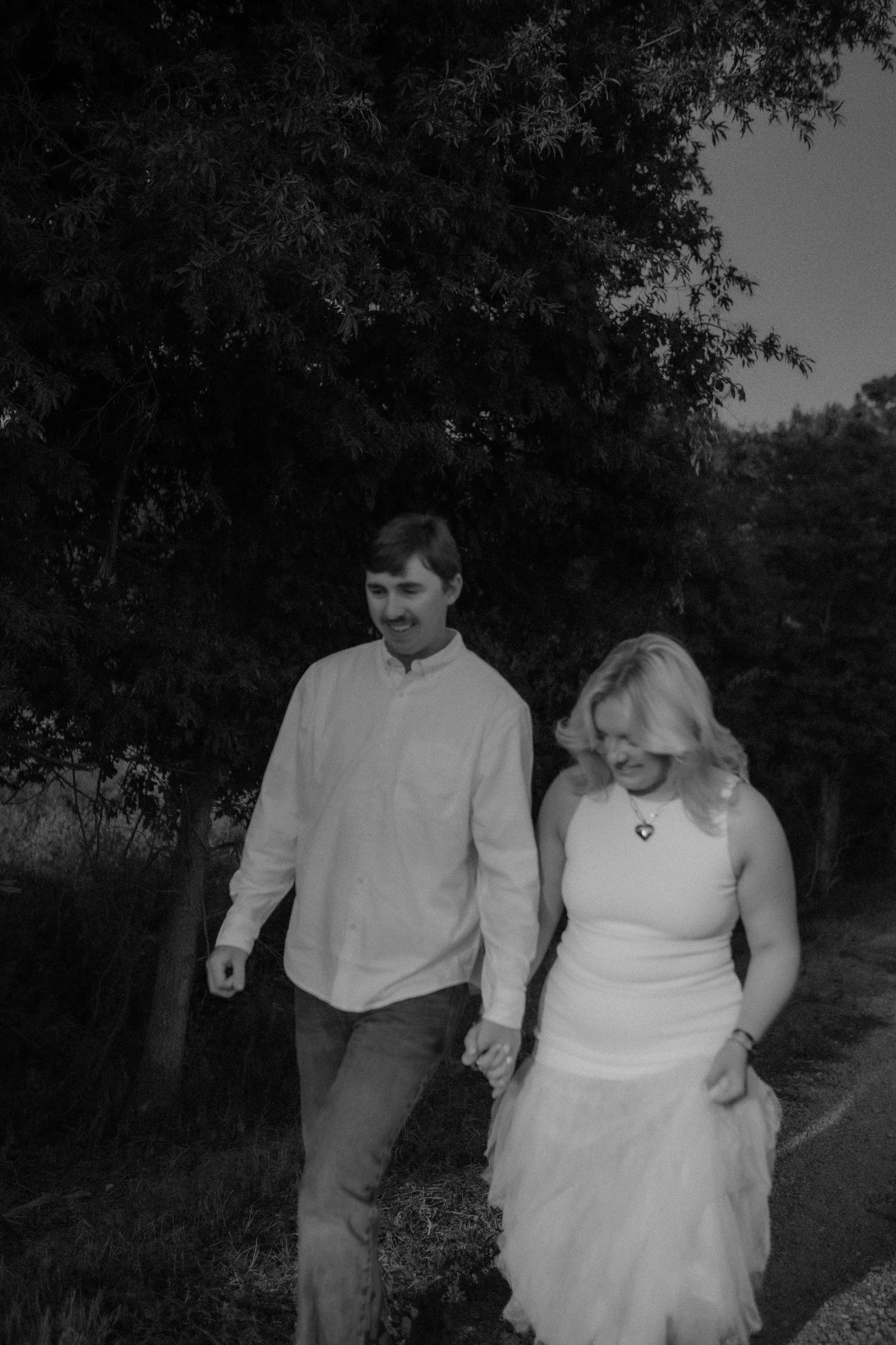 Black and white photo of couple walking hand in hand along a tree-lined path.