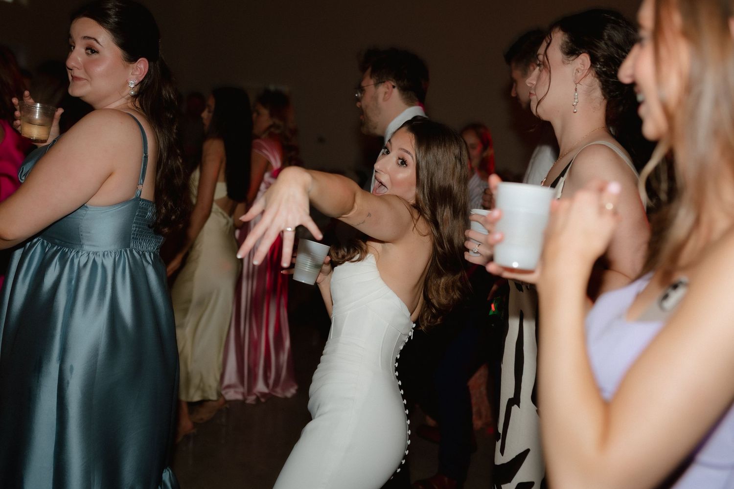 Bride in fitted white gown dancing energetically at wedding reception party.
