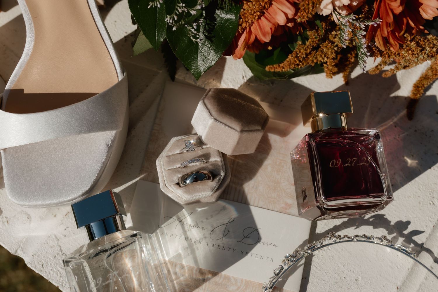 Bridal flat lay featuring white heels, ring box, pearl necklace, perfume bottles, and floral bouquet.