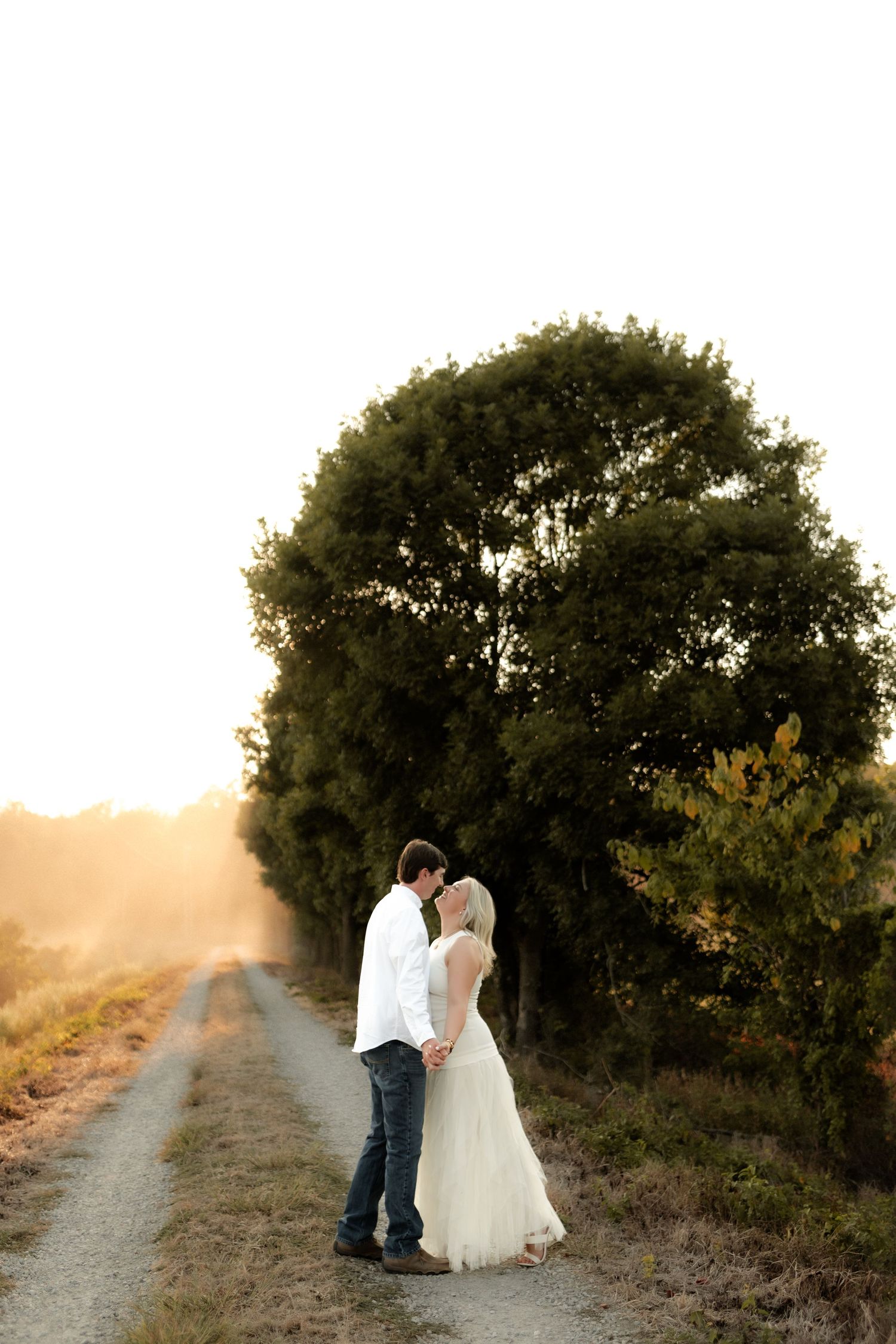 Bride and groom standing close together on a dirt path bathed in warm sunset glow.