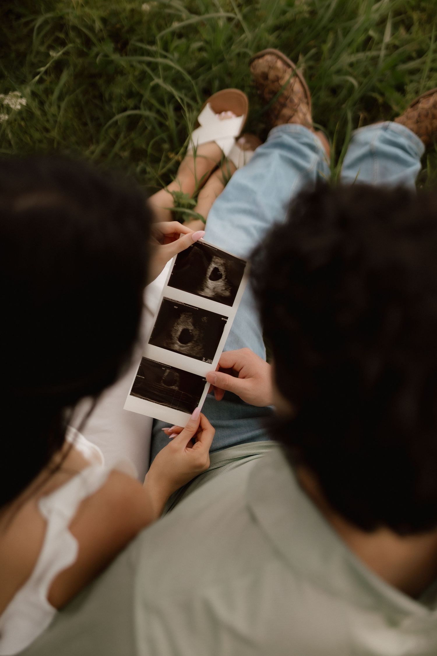 Couple sitting in grass looking at ultrasound photos together during outdoor maternity photography session.