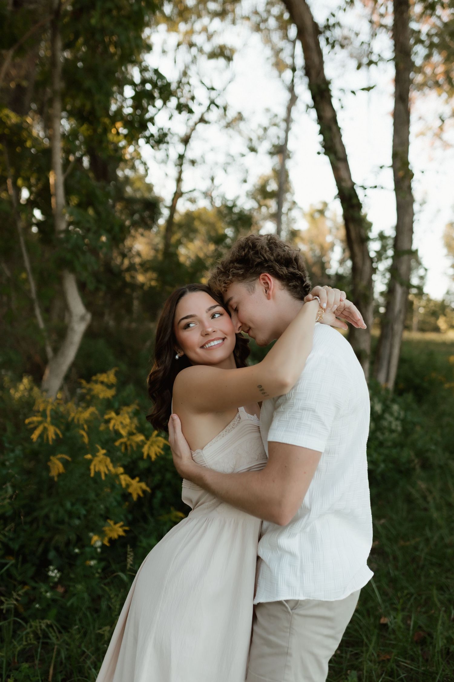 Couple sharing tender moment near yellow wildflowers, woman smiling as man kisses her cheek outdoors.