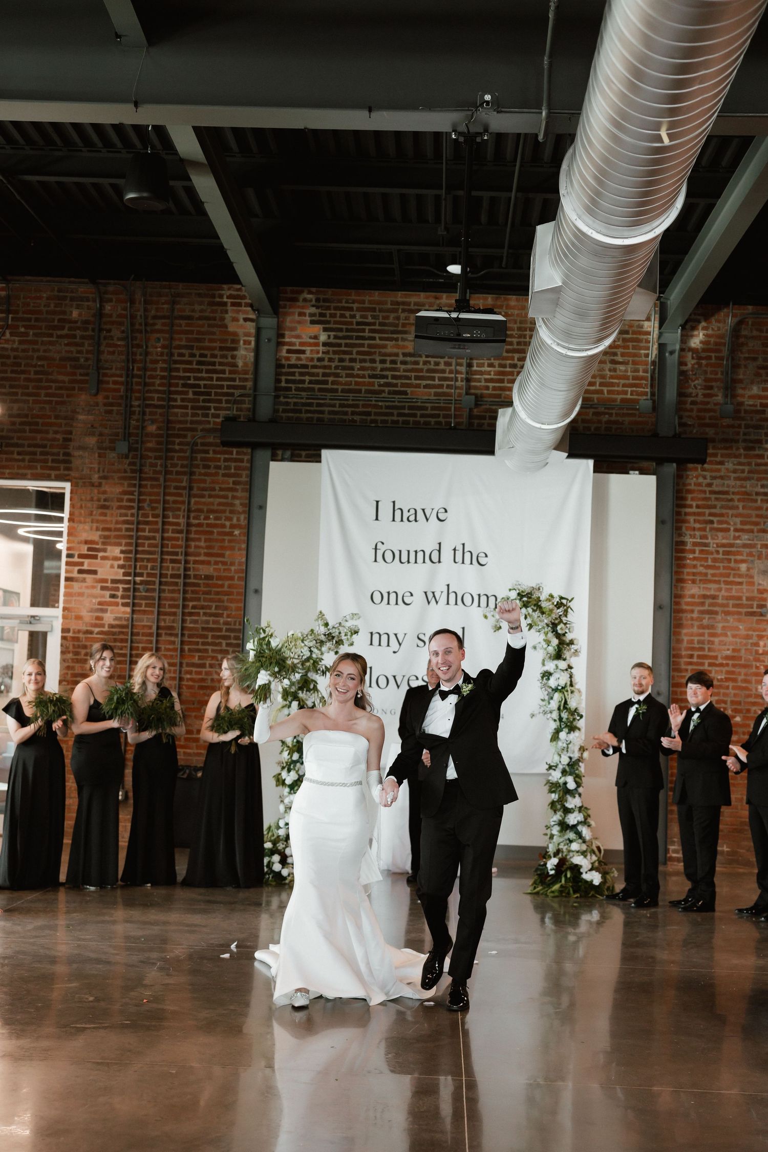 Newlyweds make grand entrance at wedding reception with floral arch backdrop.