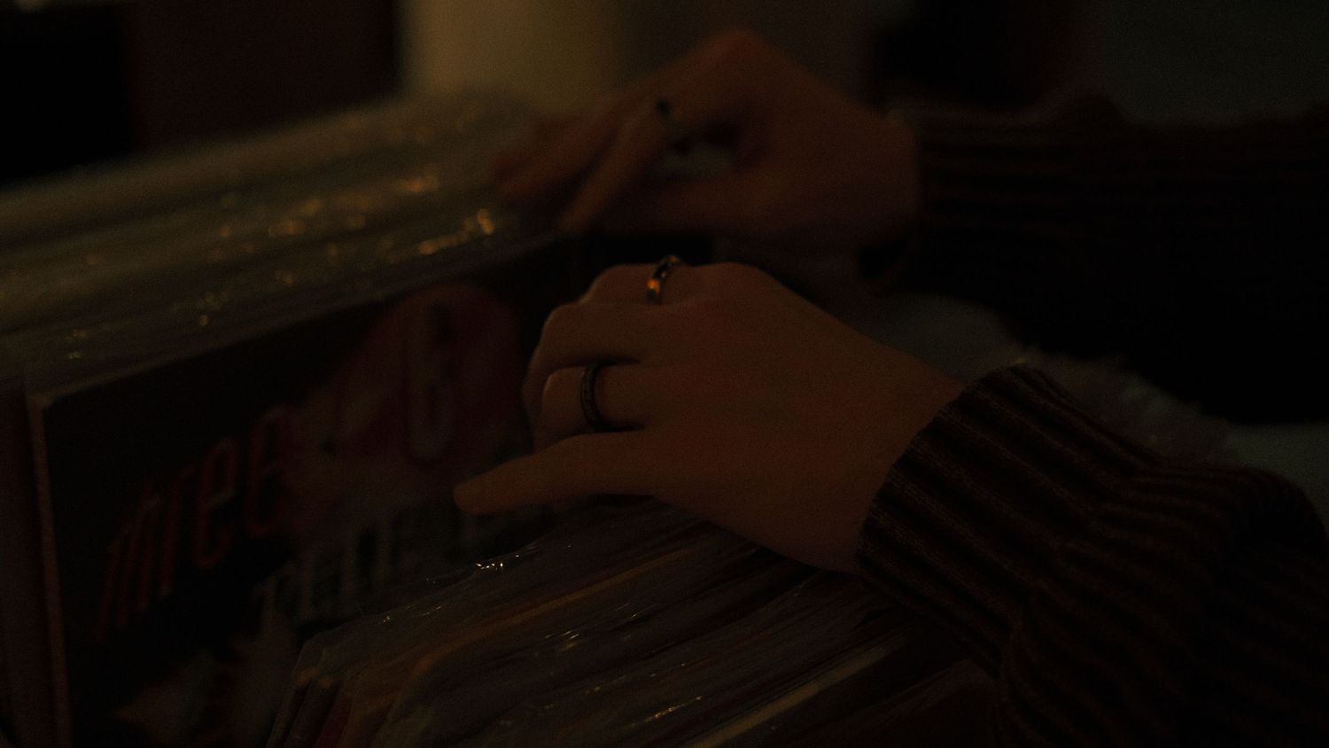 Close-up of hands with ring browsing vinyl records in dim warm lighting.