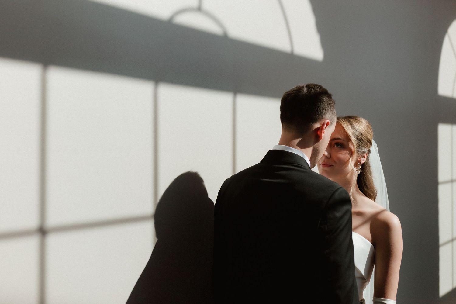 Bride and groom share a romantic moment bathed in soft natural window light.